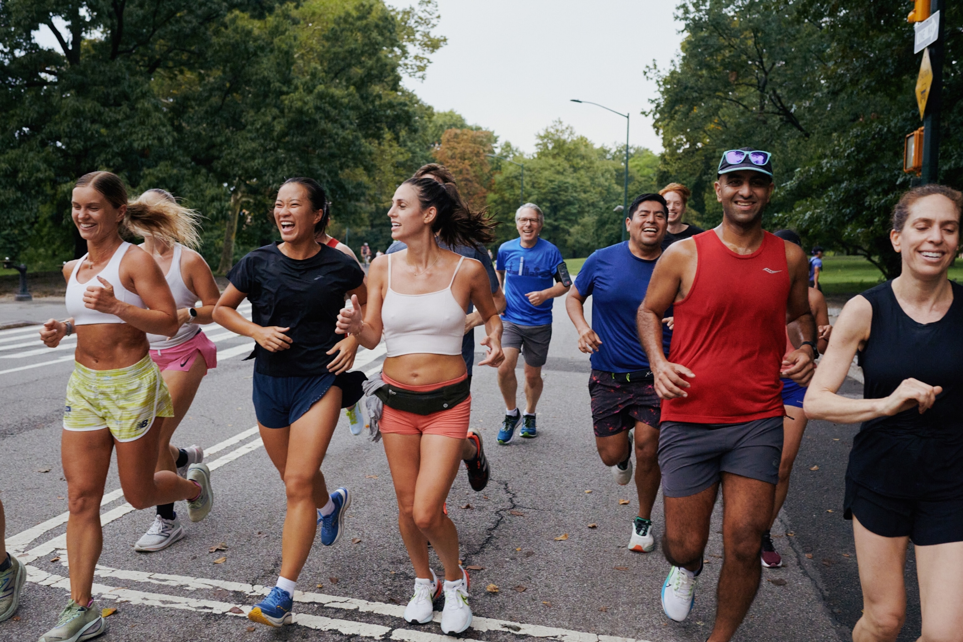 A group of runners, many of whom are smiling, as they run along an otherwise empty street.