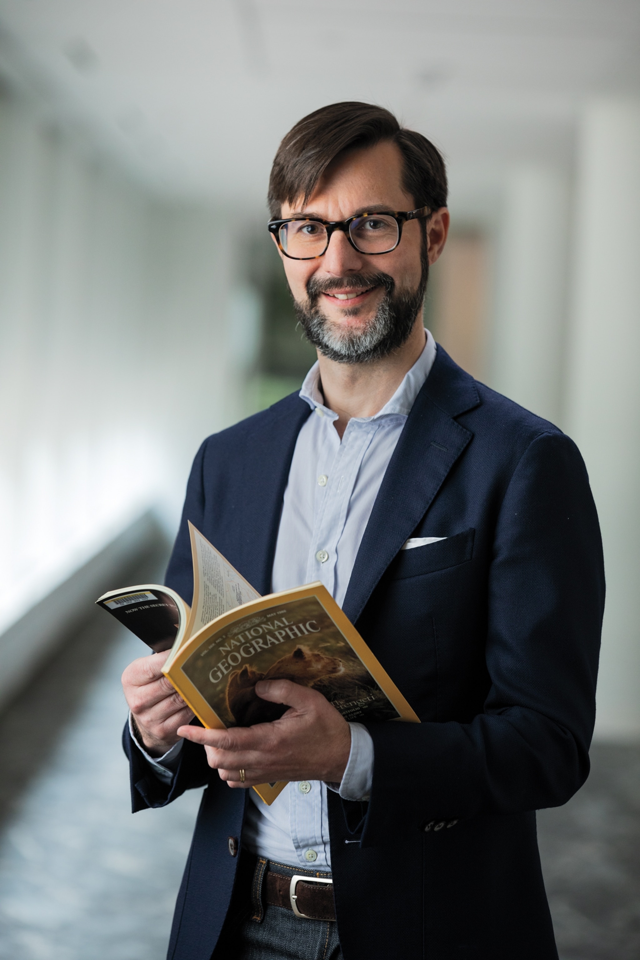 Picture of smiling man in suit and eyeglasses holding magazine.