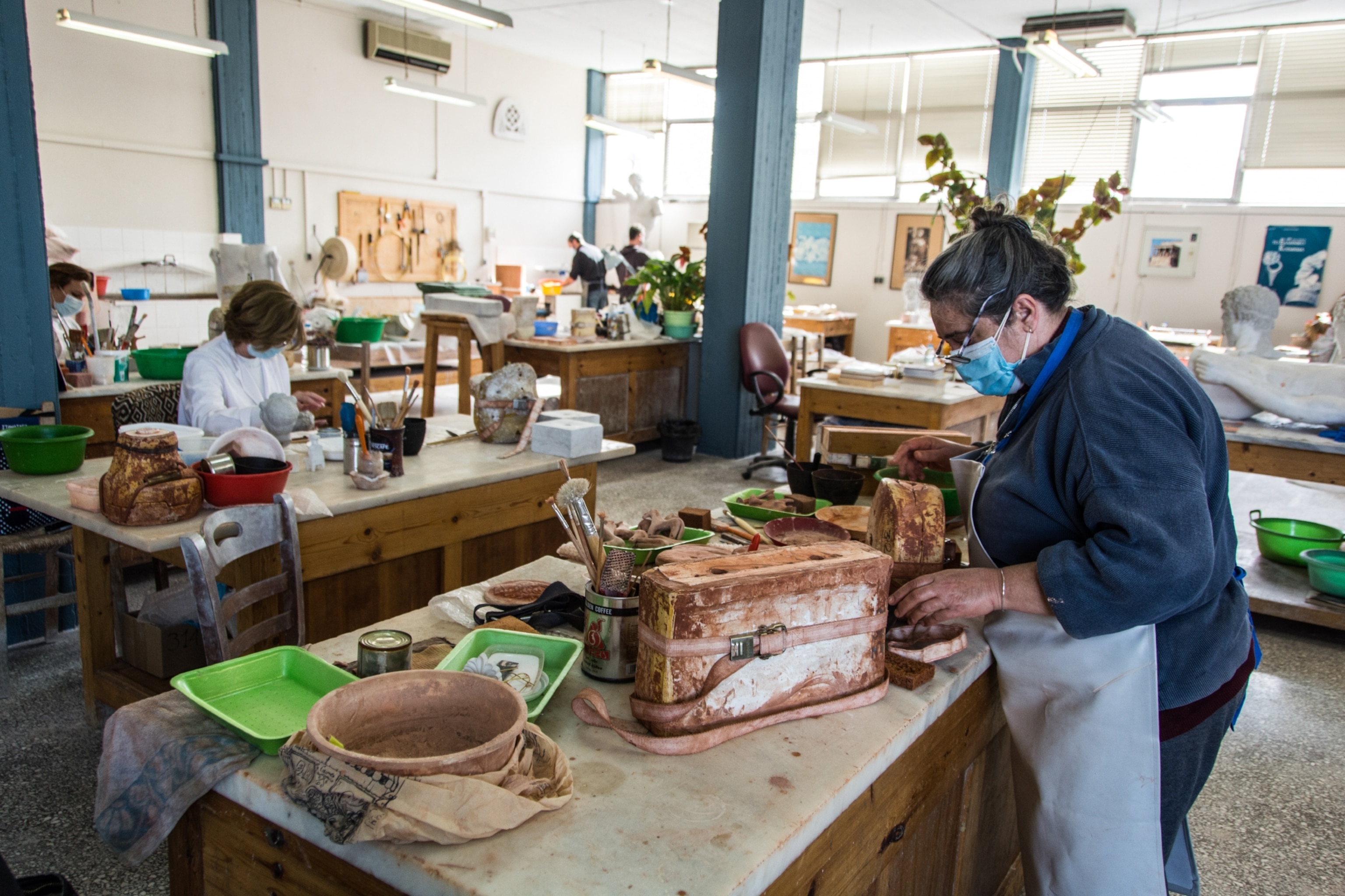 Several artists work in a shop constructing replicas of fine Greek art
