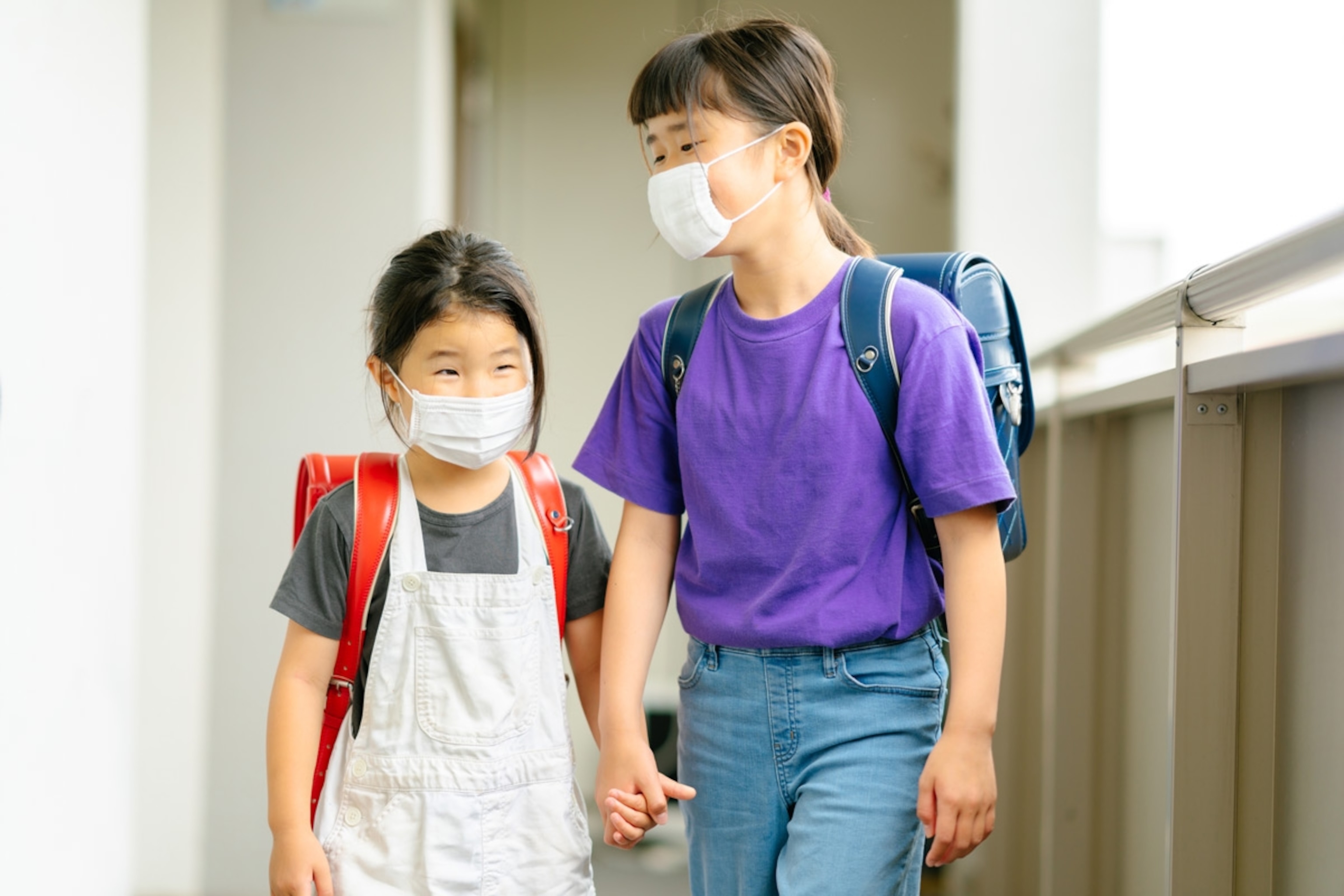 Elementary age sisters are wearing protective face masks and going to school together. (Japan)