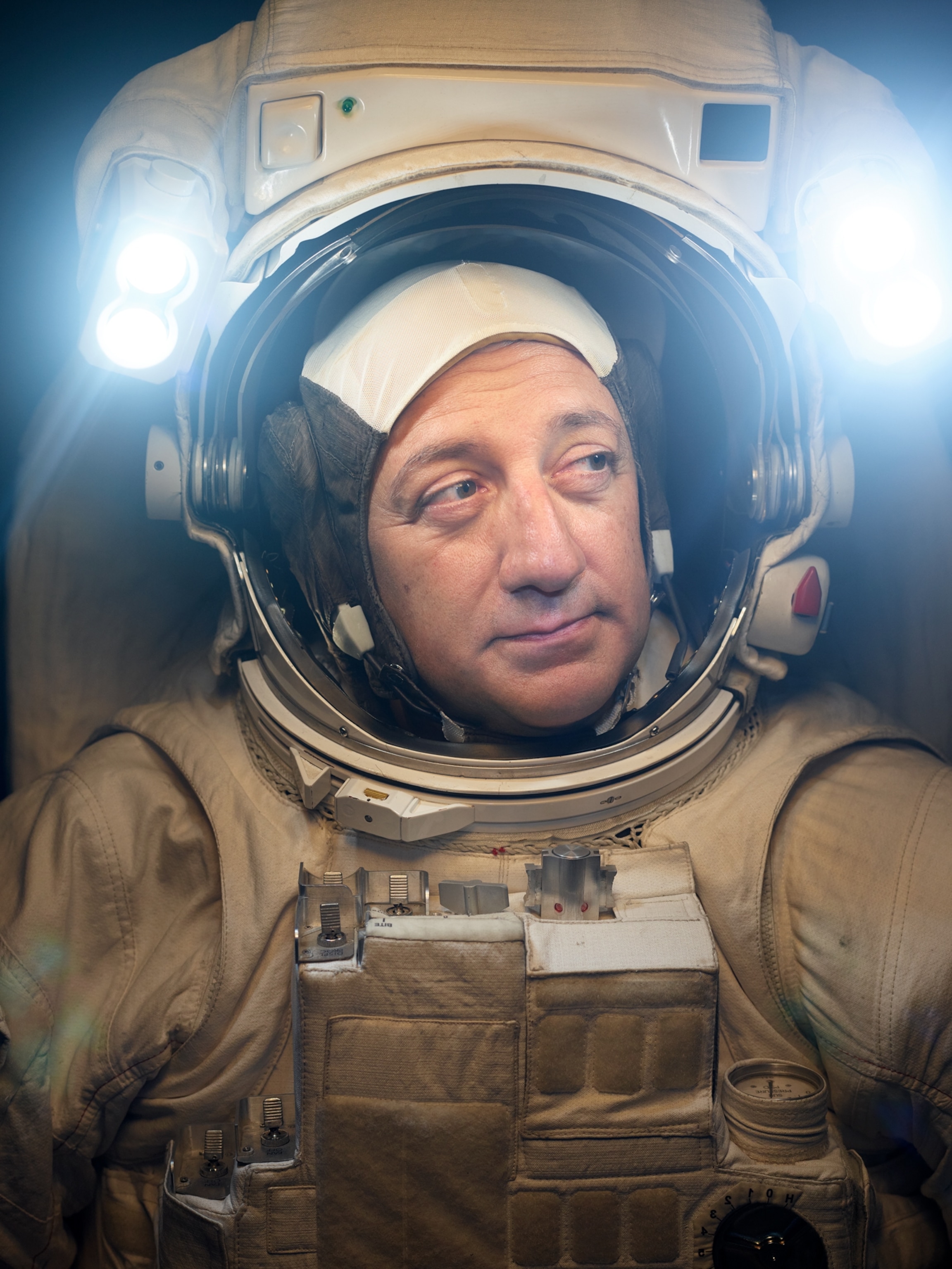 Mike Massimino tightly framed in a white astronaut suit with the lights on.