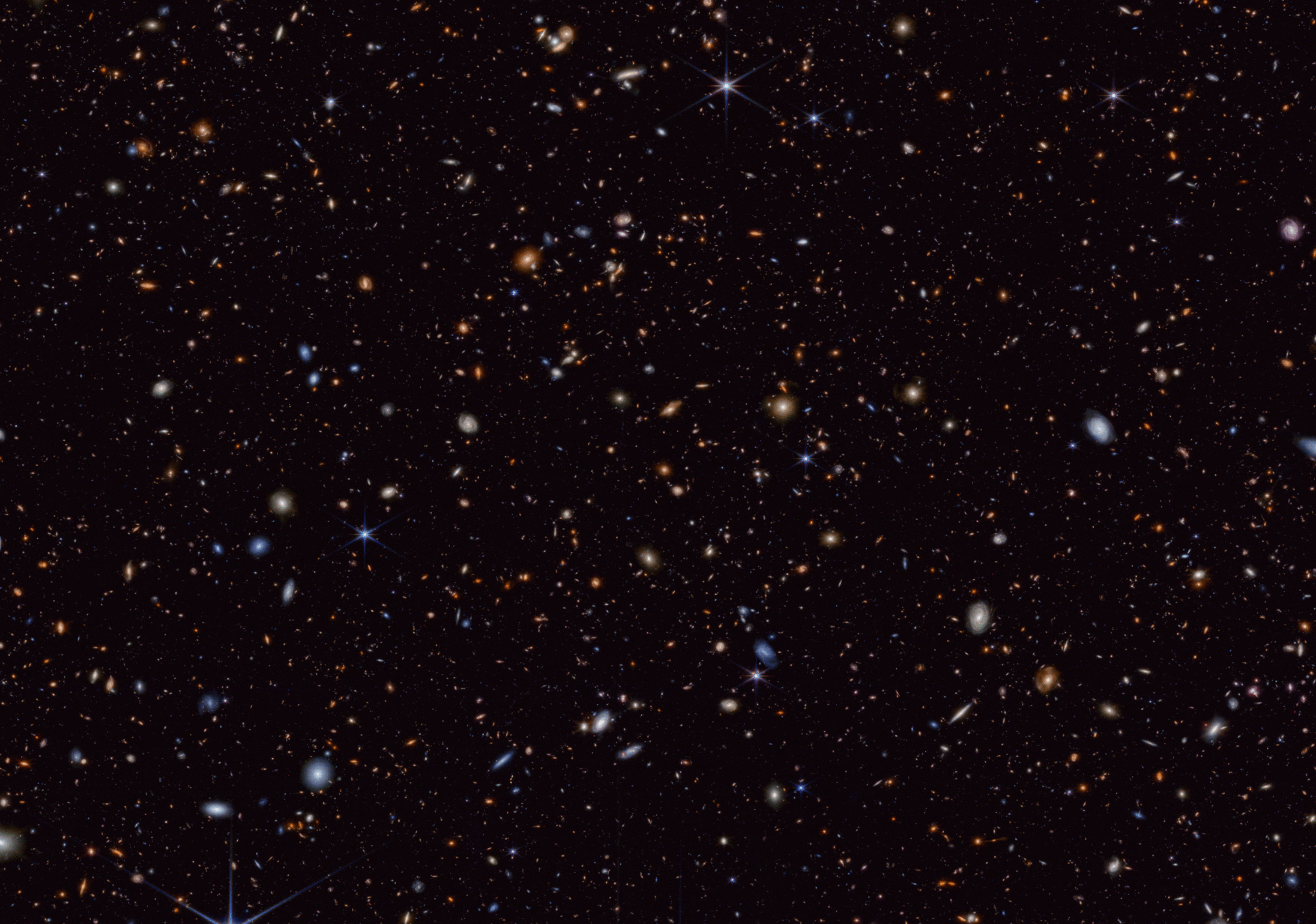 Space telescope image showing hundreds of objects of different colors, shapes, and sizes scattered across the black background of space. There are small red blobs; larger, fuzzy white or blueish ball-shaped masses with bright centers; white, pink, or blue disc shapes; clear spiral structures; and barely discernible specs. Eighty-three of the smaller objects in the image are circled in green. Some of the circles are close together; some are far apart; some overlap. There is no apparent pattern in the distribution.