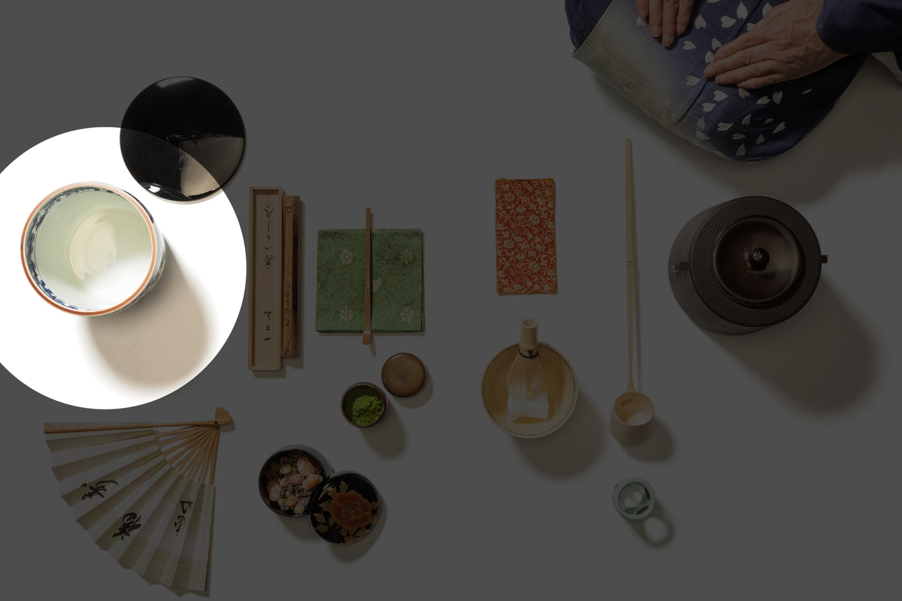 Picture of tea ceremony set of dishes and utensils and woman's hands resting on laps.