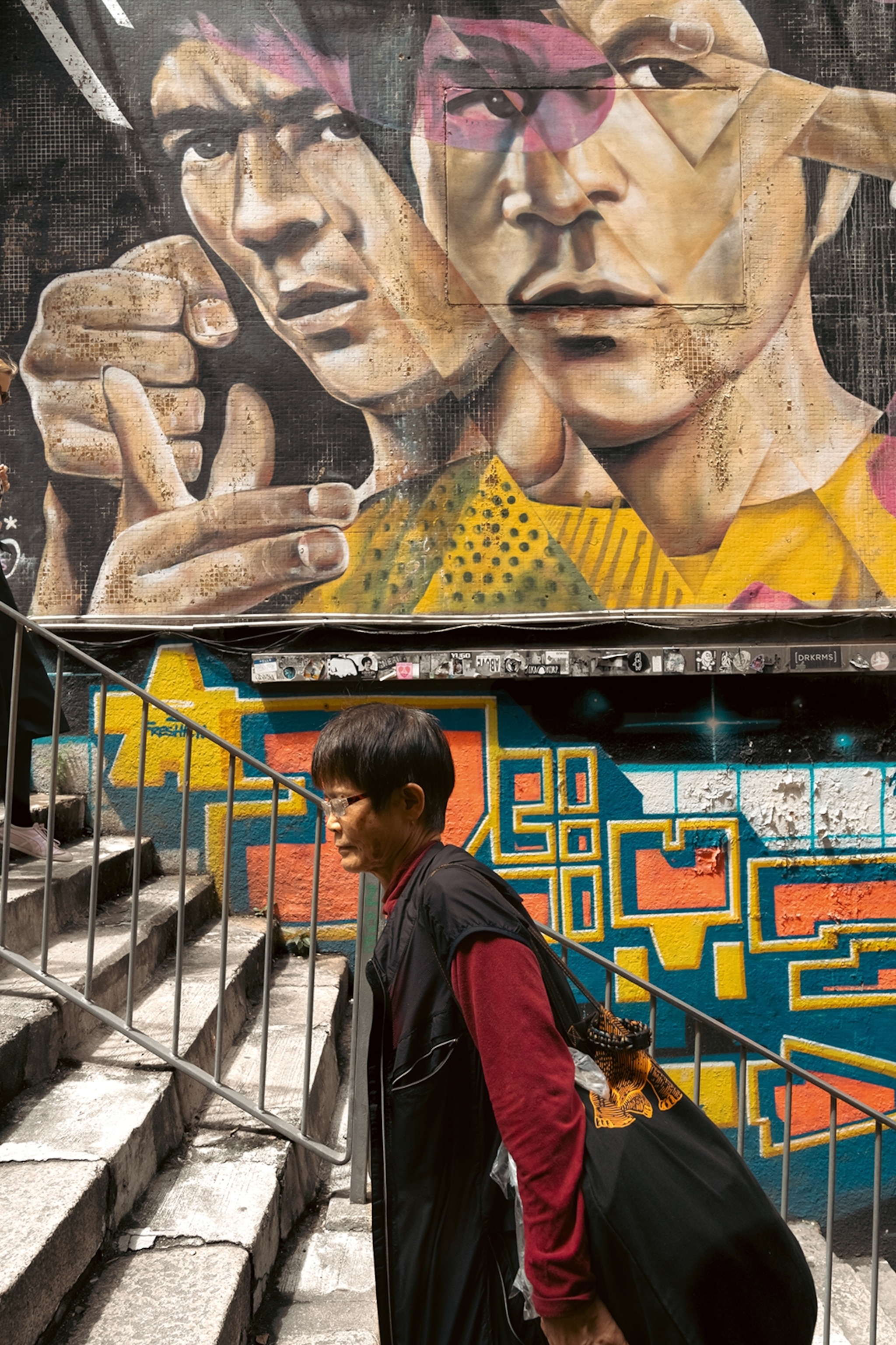 A woman walking up the stone steps past an impressive mural of actor Bruce Lee.