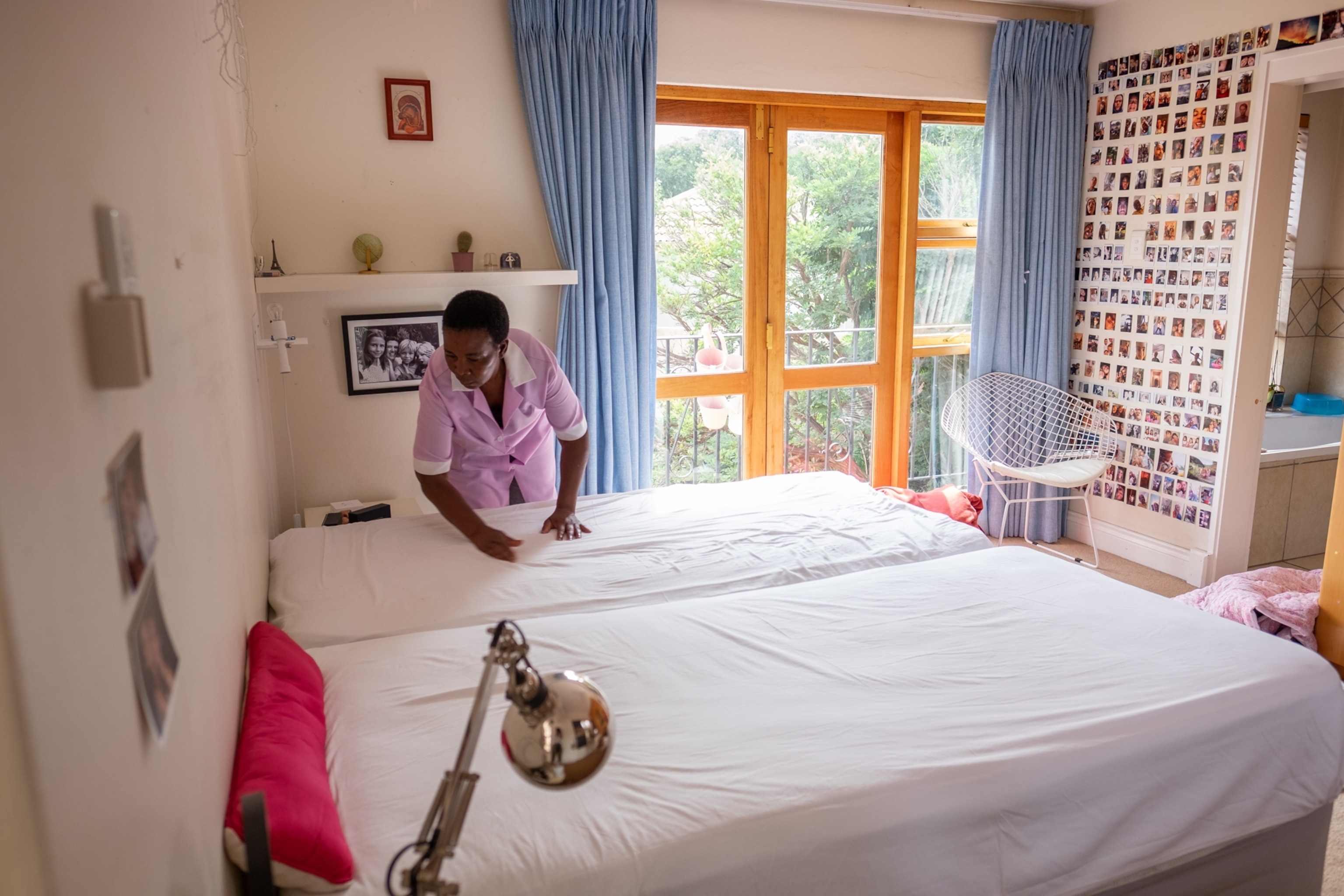 a woman making a bed in a sun lit room