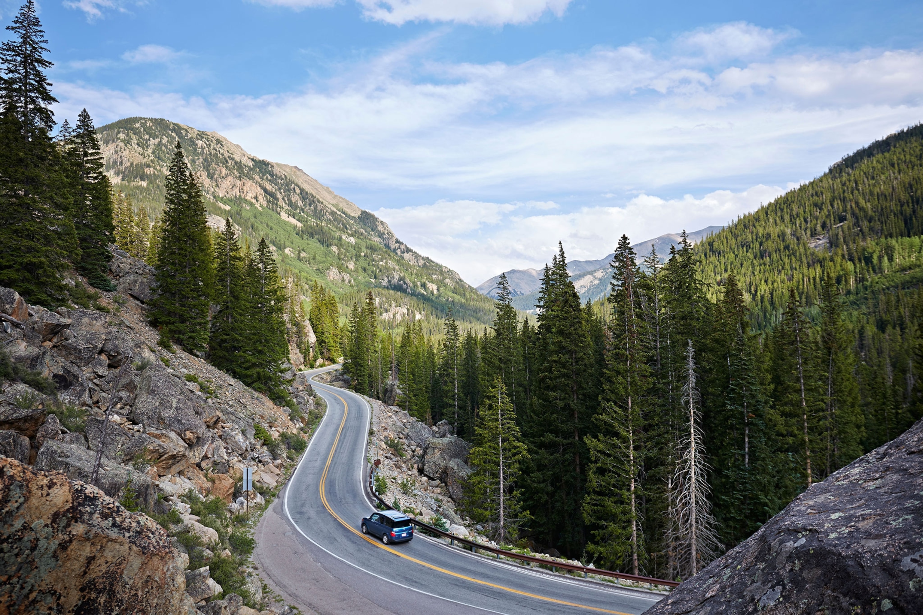 Car on winding on highway in the mountains, with towering trees in Aspen, Colorado, USA