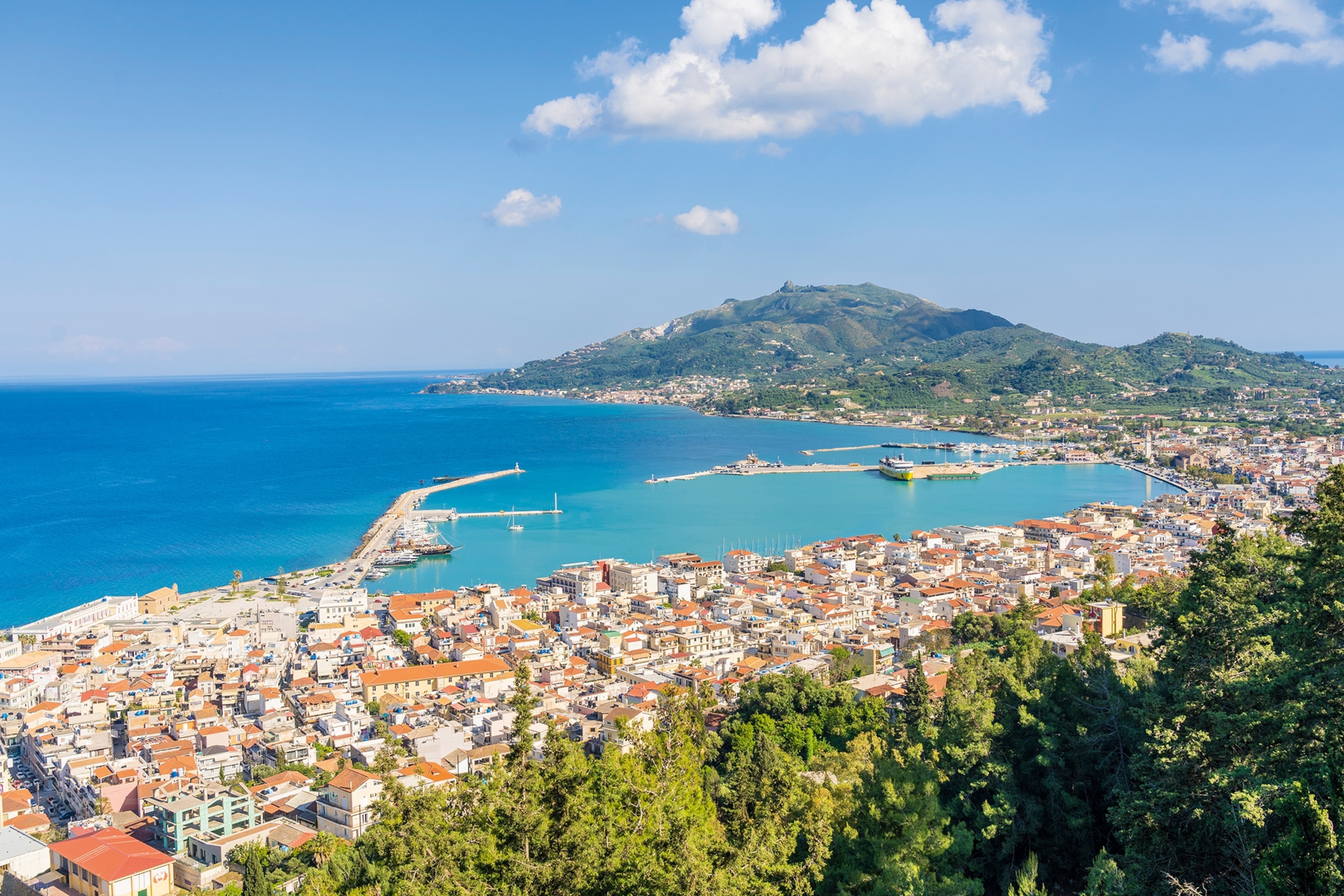 A birds-eye view on a coastal Greek town with harbour arms reaching out into the sea.