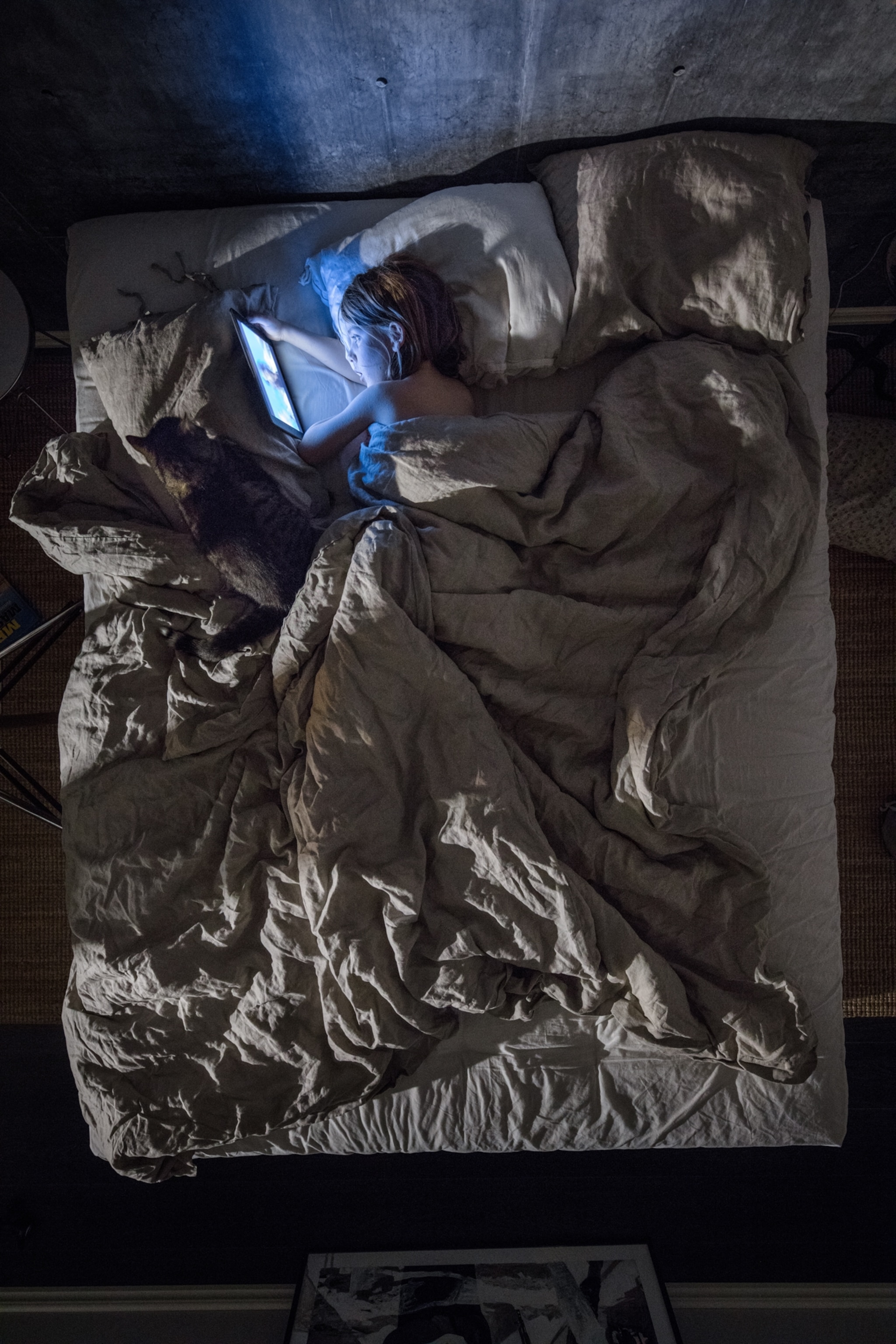 an aerial view of a young boy in bed looking at an iPad emitting bright blue light