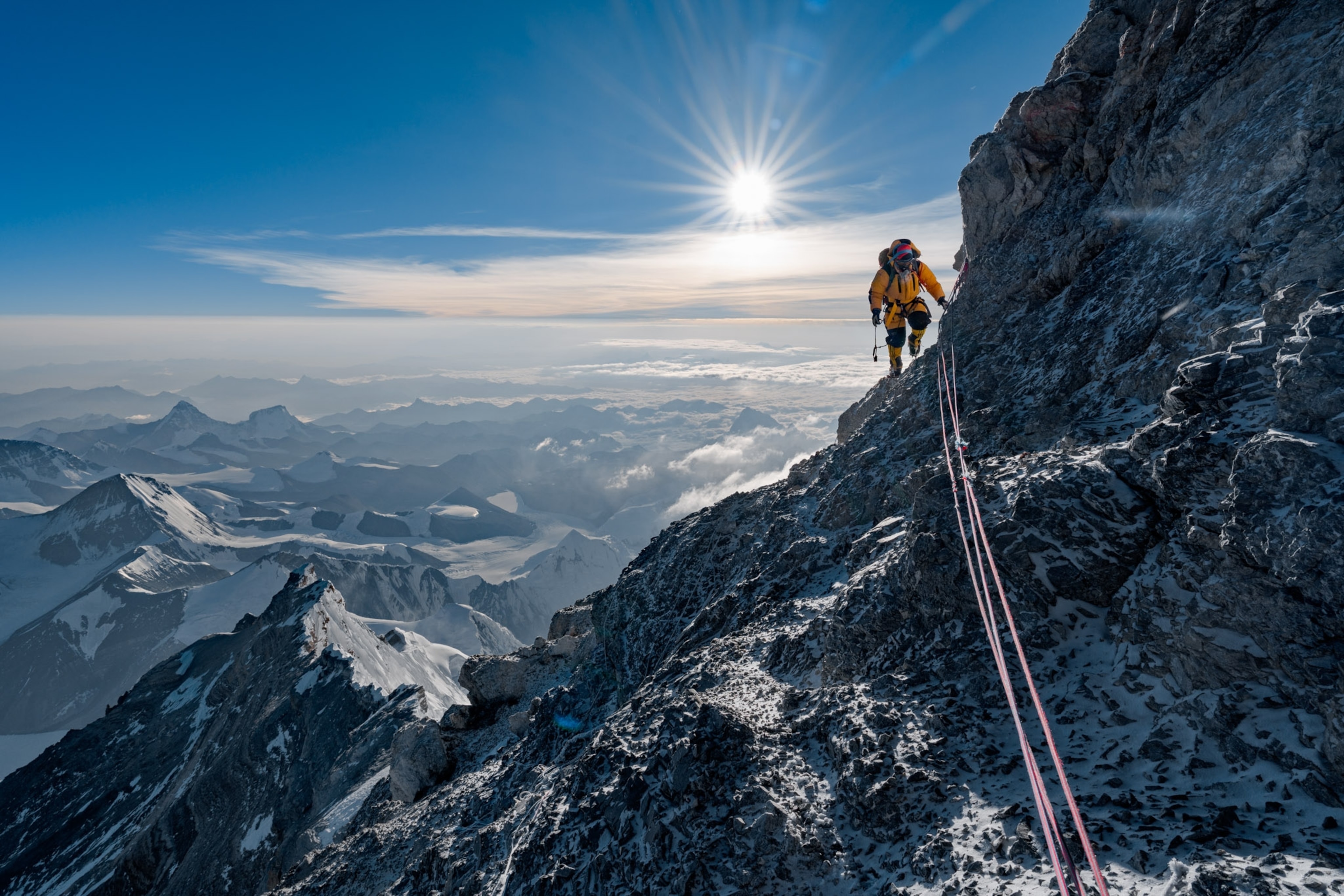 a man in a yellow snowsuit on the edge of a steep rocky mountainside