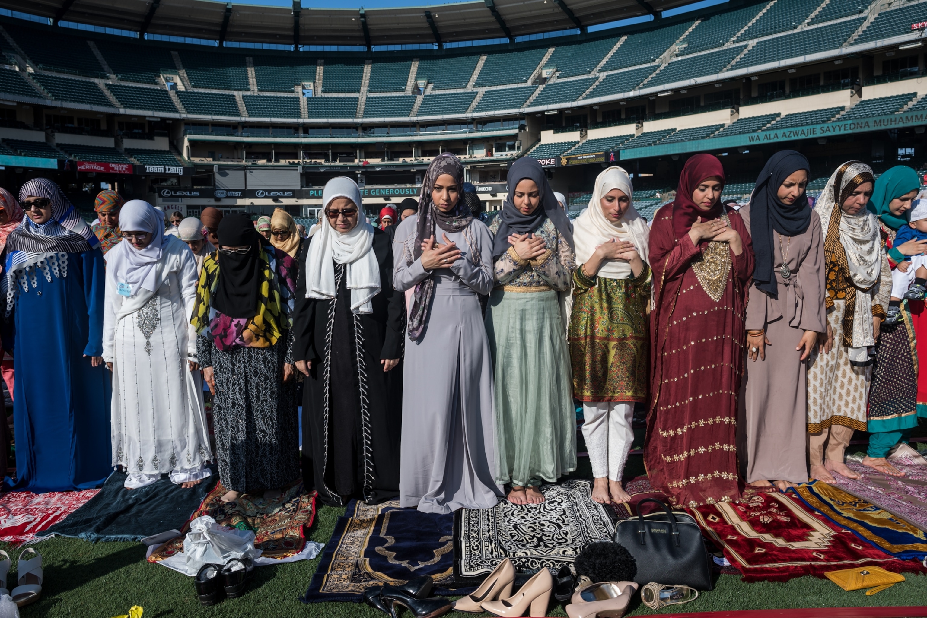 hijabi women praying inside a large open stadium during the day