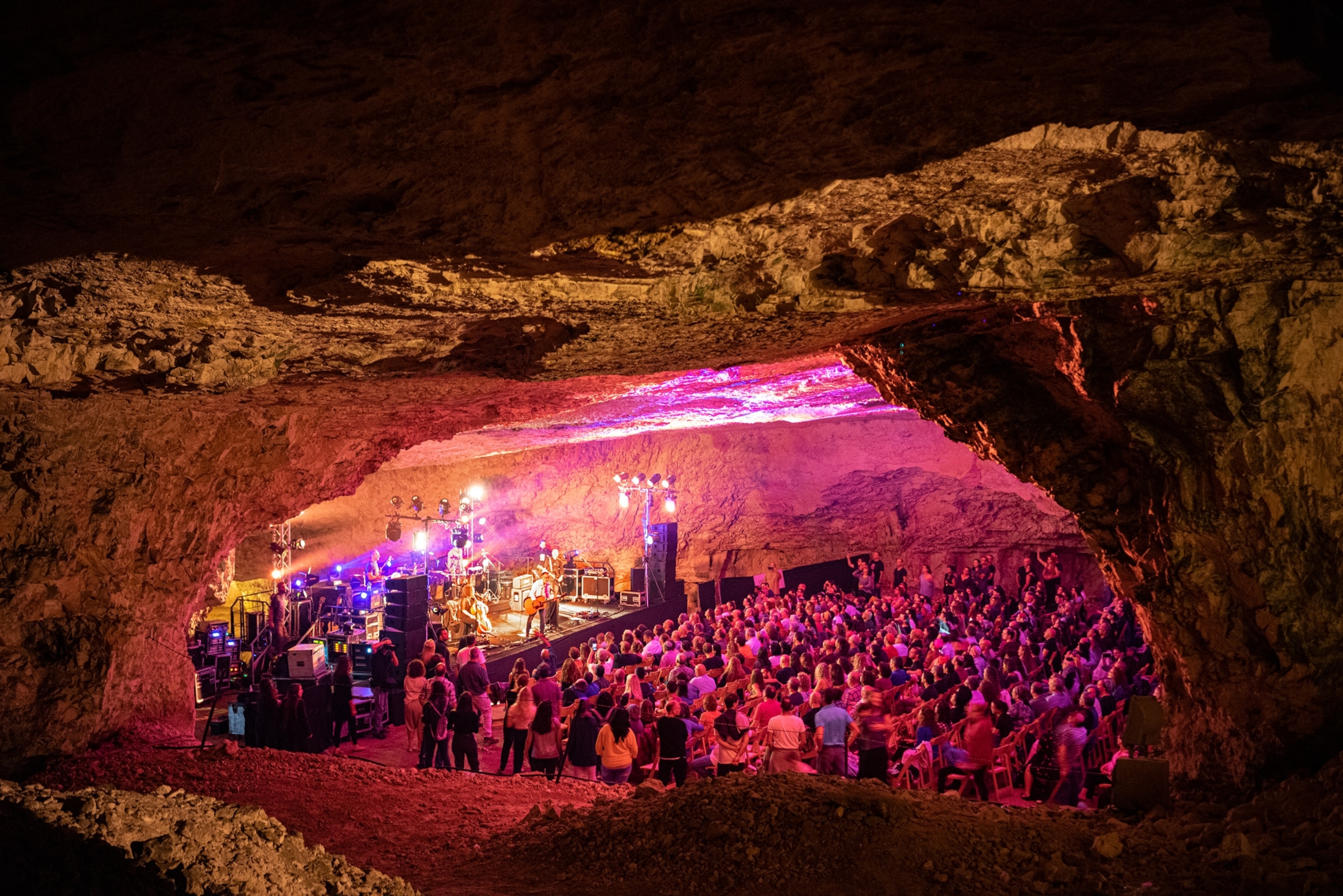 people underground in a cave listening to a concert under pink neon lights