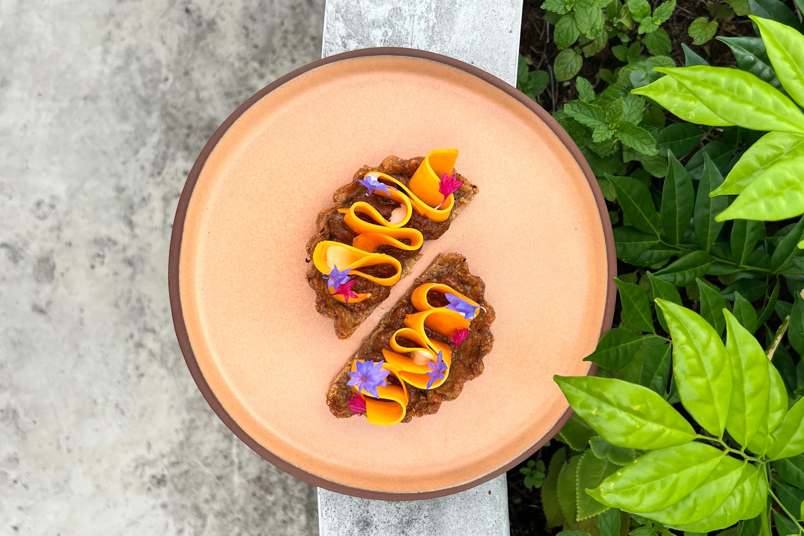 A plate of two tart slices topped with a wriggly strip of pumpkin and edible flowers