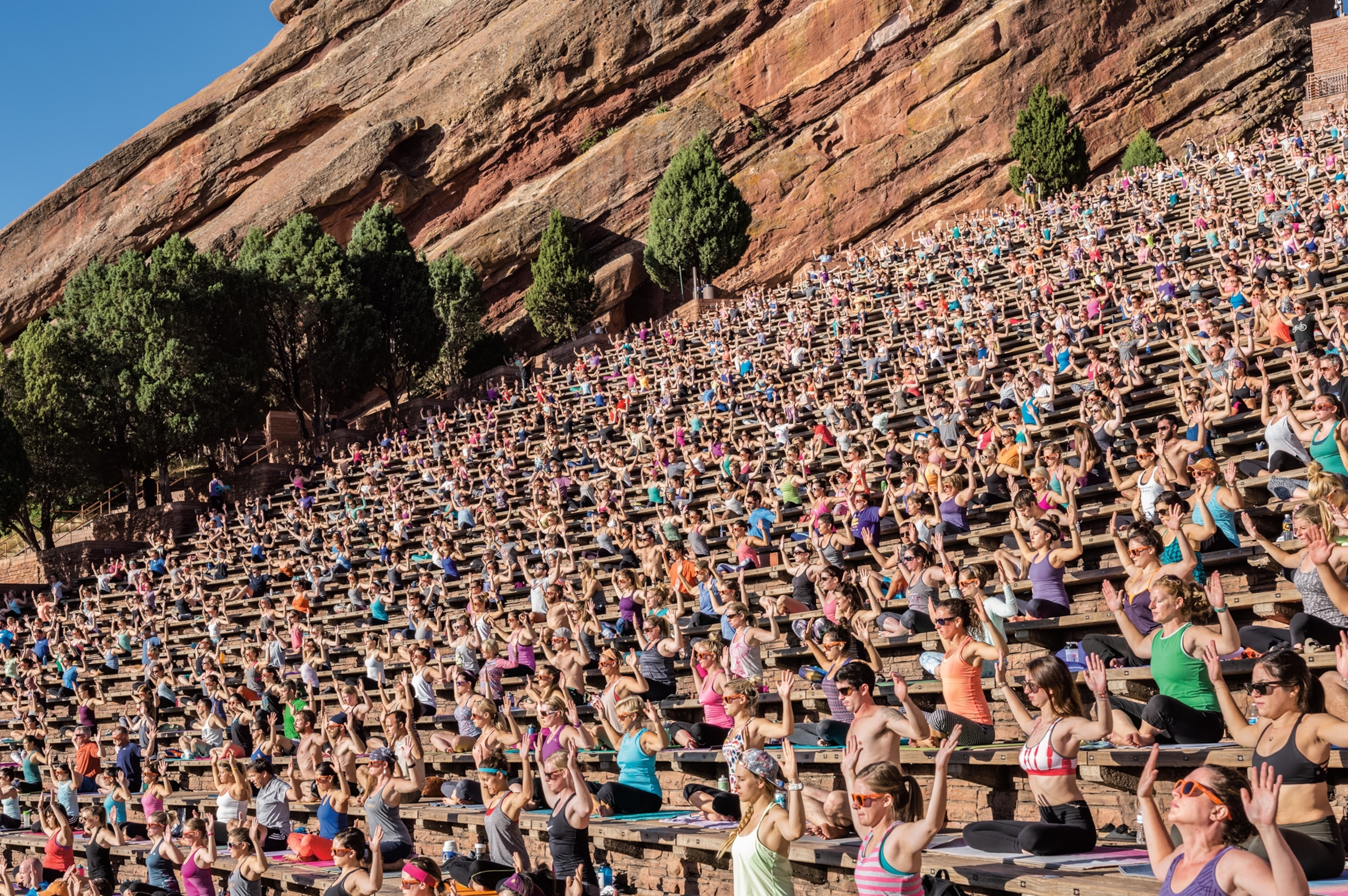amphitheater full of people in yoga pose facing sun with hand up.