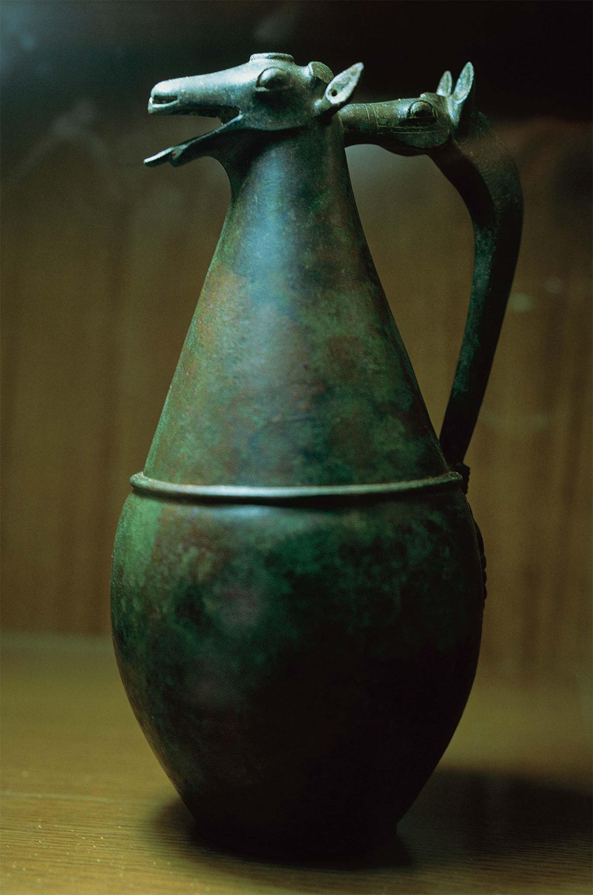 A bronze jug is topped with a deer’s head and has a handle shaped like a horse’s head