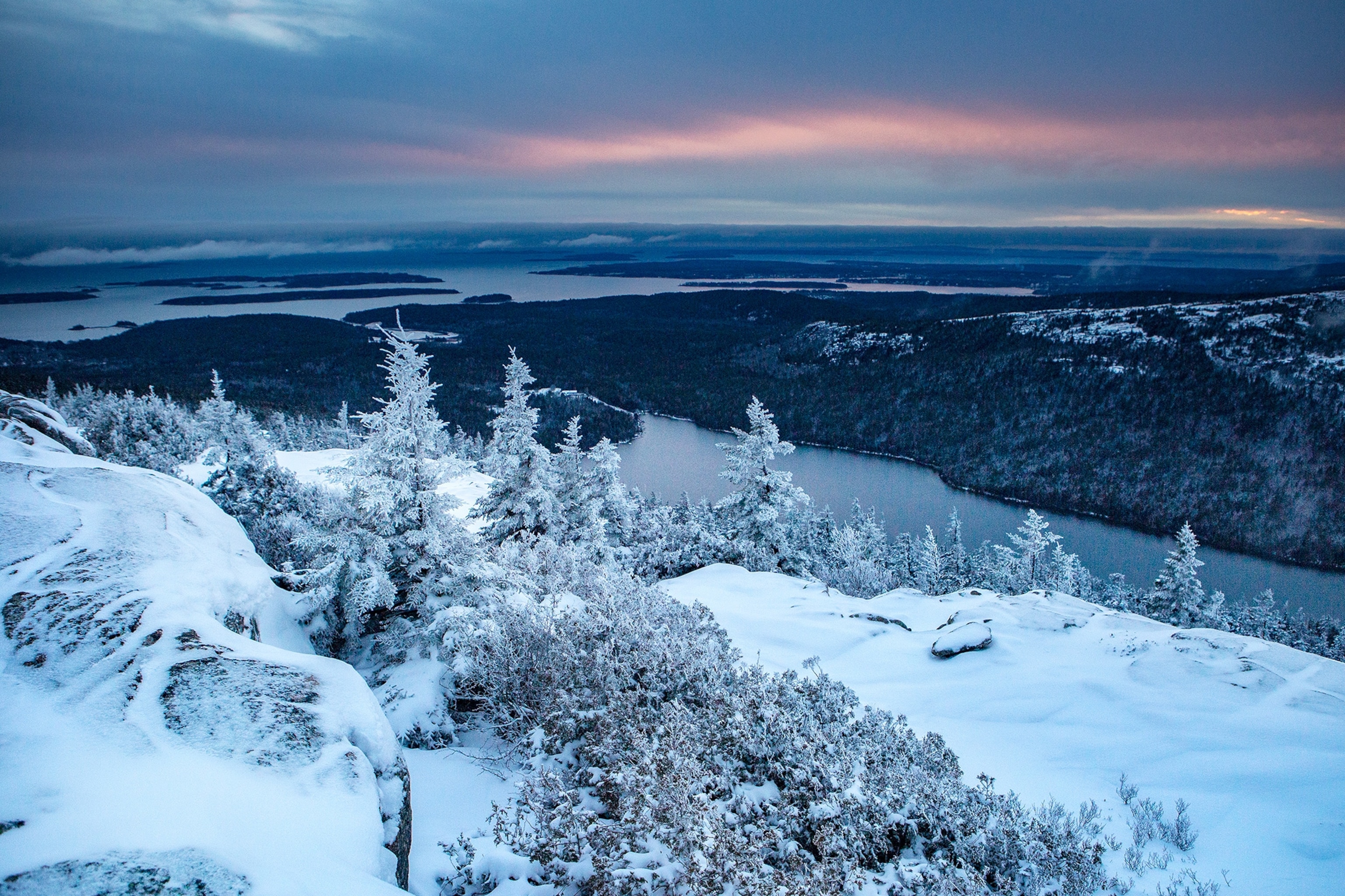 The sun sets while fog hangs over Penobscot Mountain from Pemetic Mountain in Acadia National Park.