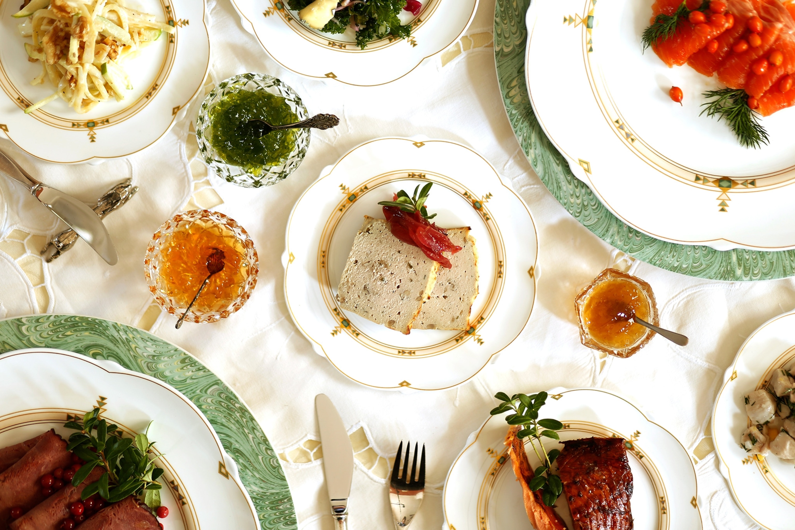 An elaborately set table with Cured salmon with buckthorn, kale pesto, Pâté de champagne with pickled red onion, apple & calvados gelé, juniper berry gelé, and Waldorf salad prepared by Tertin Kartano.