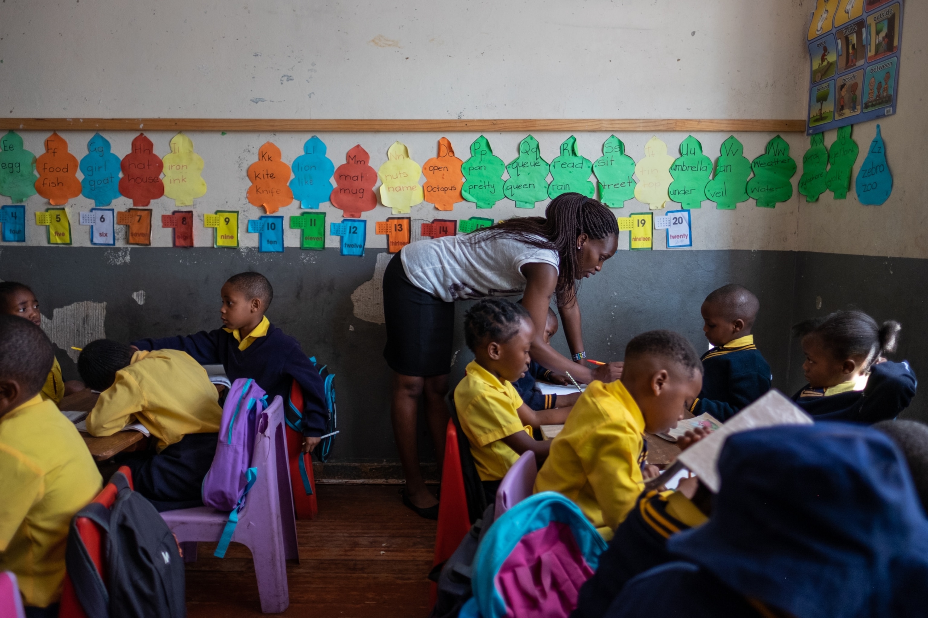a woman leaning over a table filled with schoolchildren working