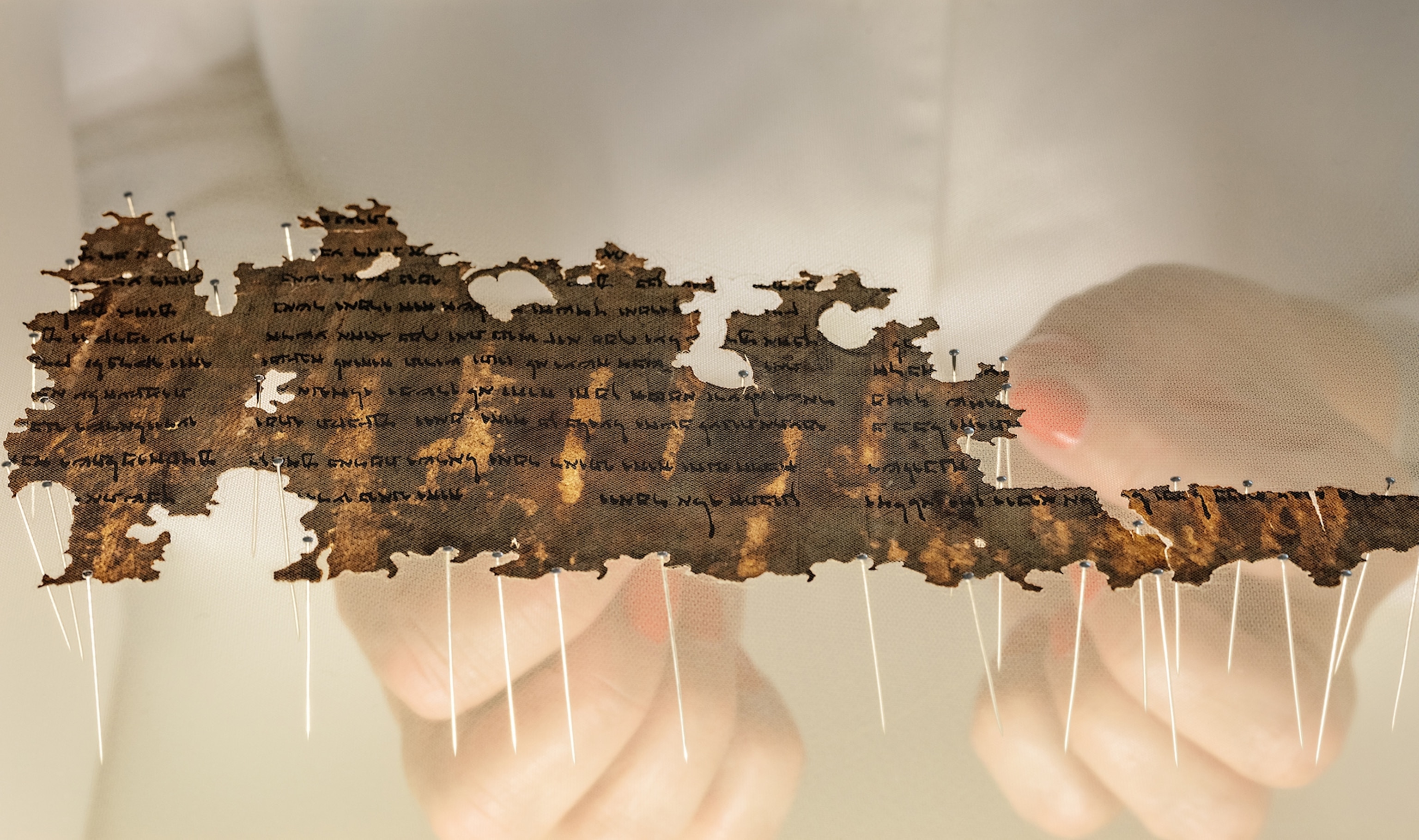 a scroll fragment in conservator's hands