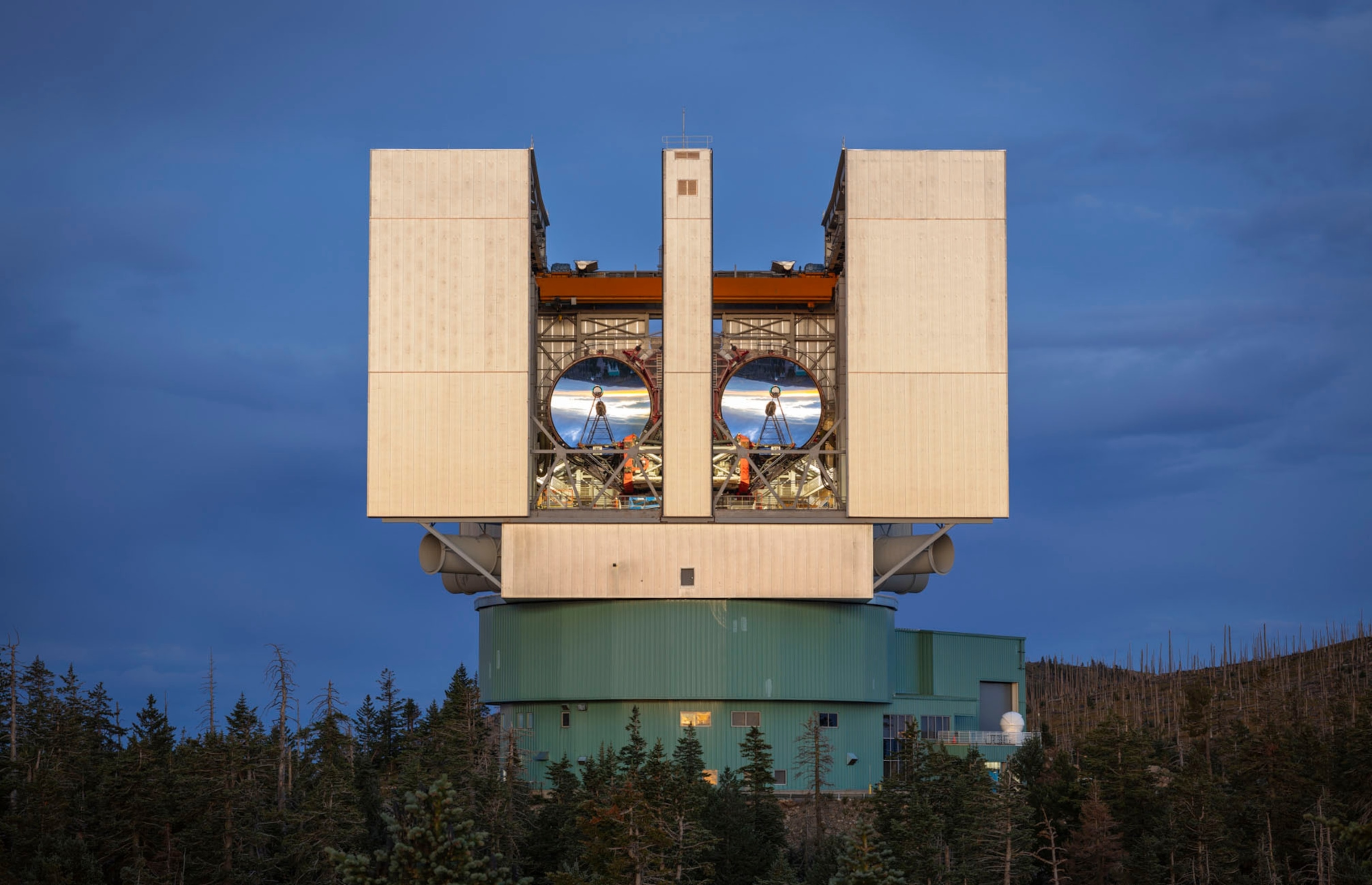 a large building that iis wider on top than on bottom holds two huge silver parabolic lenses on the front side aimed in a similar direction.