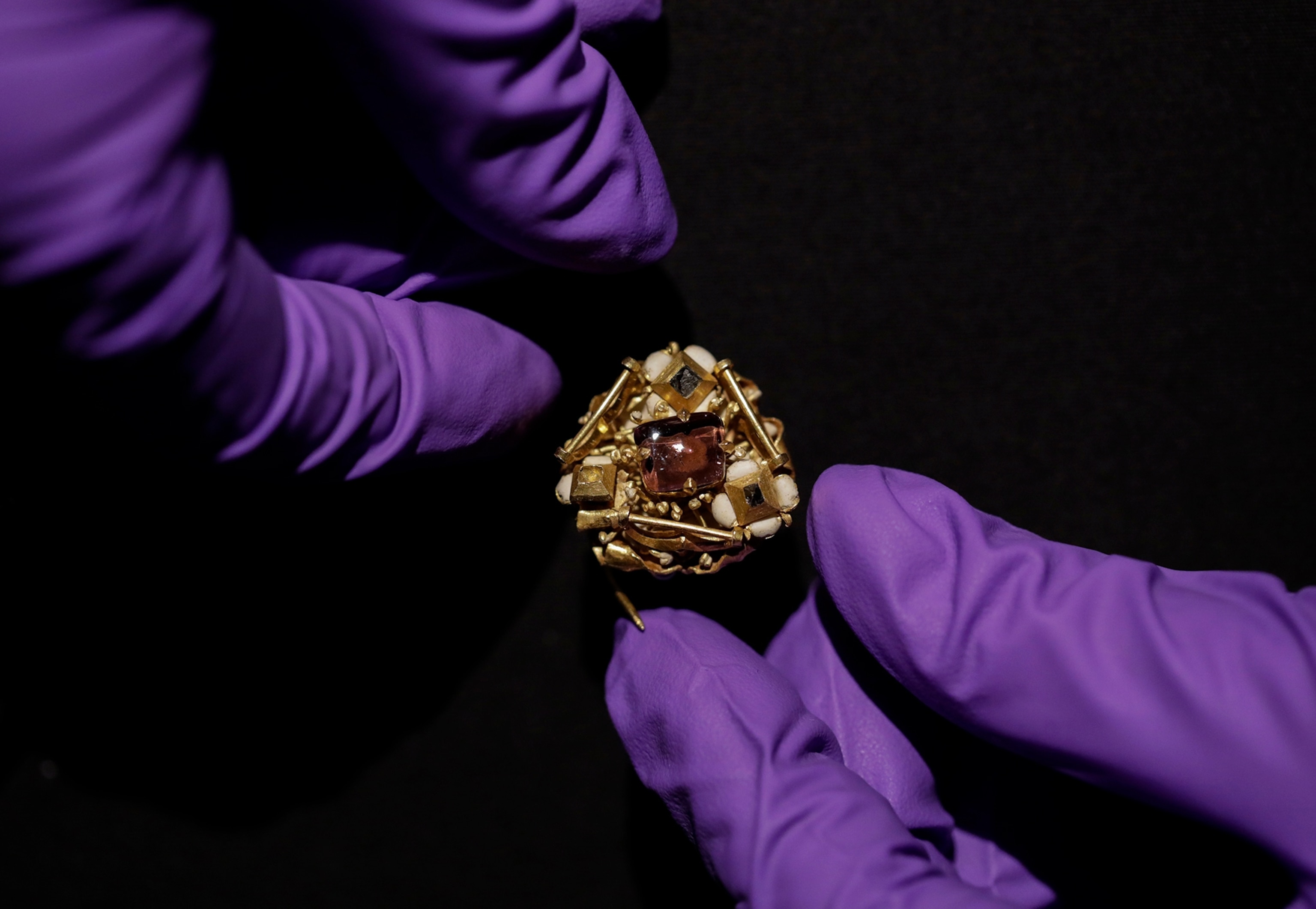 A purple globed hand holds a jewelled late Medieval cluster brooch.