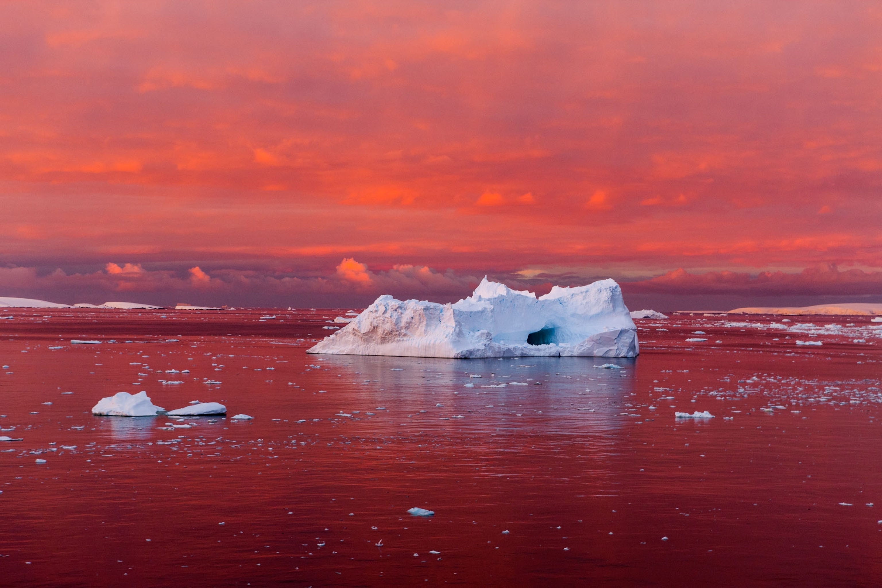 a red sunset reflecting on the water with stark white ice chunks floating
