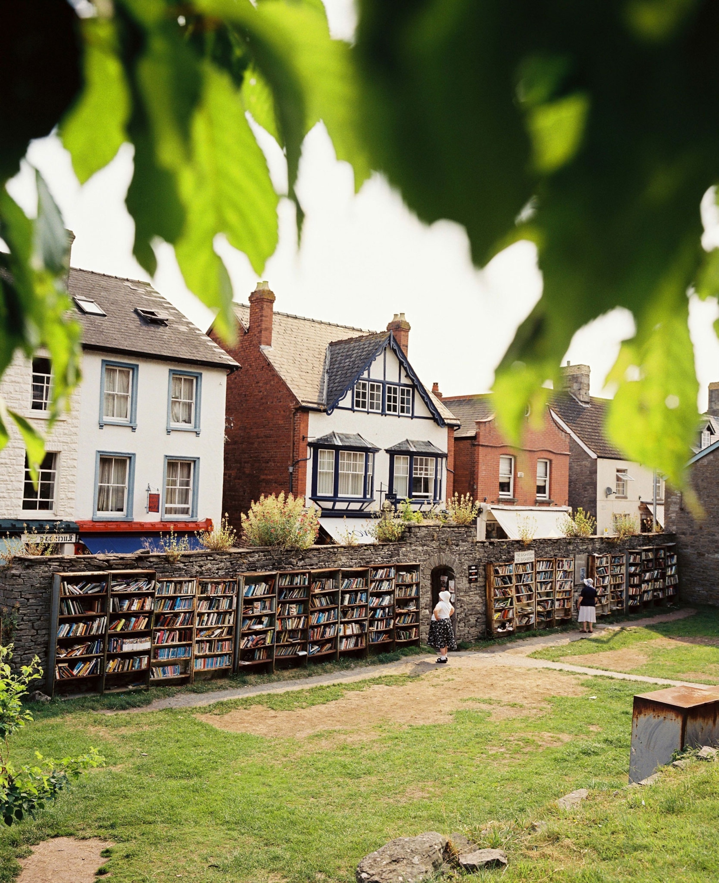Village homes with a brick wall guarding them. The brick was has dozens of  shelves that are filled with books.