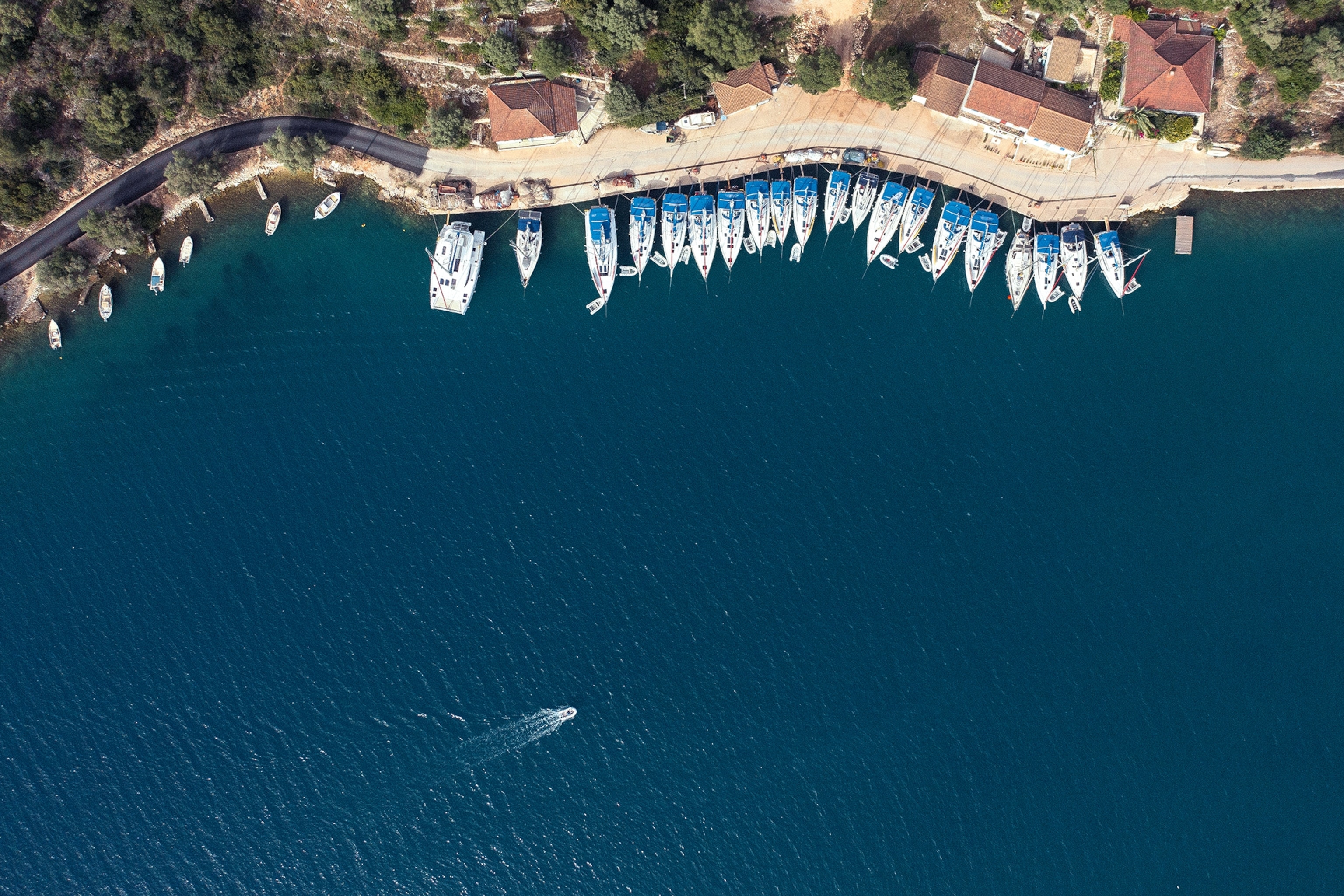 A birds-eye view on a harbour with similar sized boats lined up on the coastline.