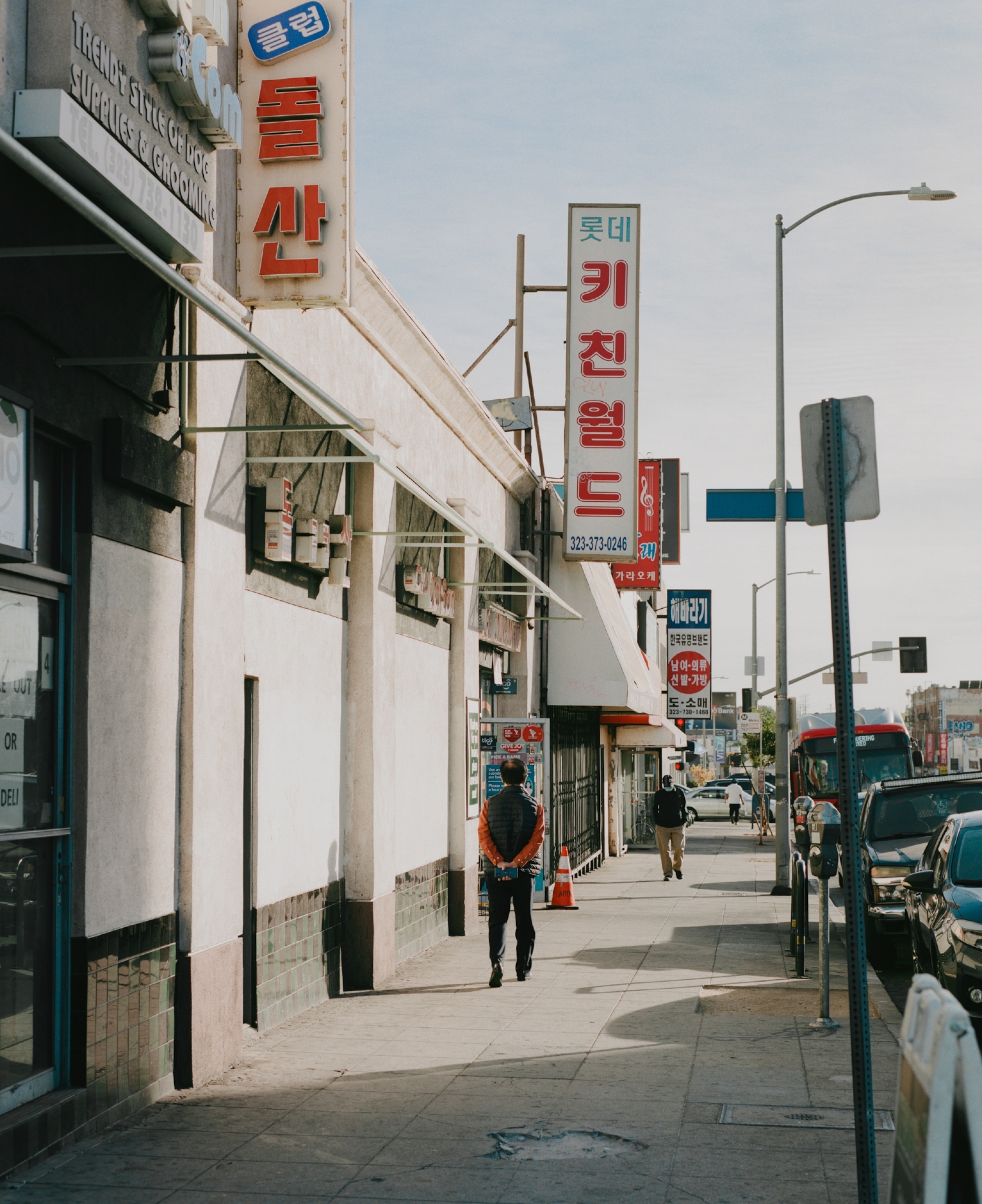 A man walks down a sidewalk lined with storefronts signs written in Korean language