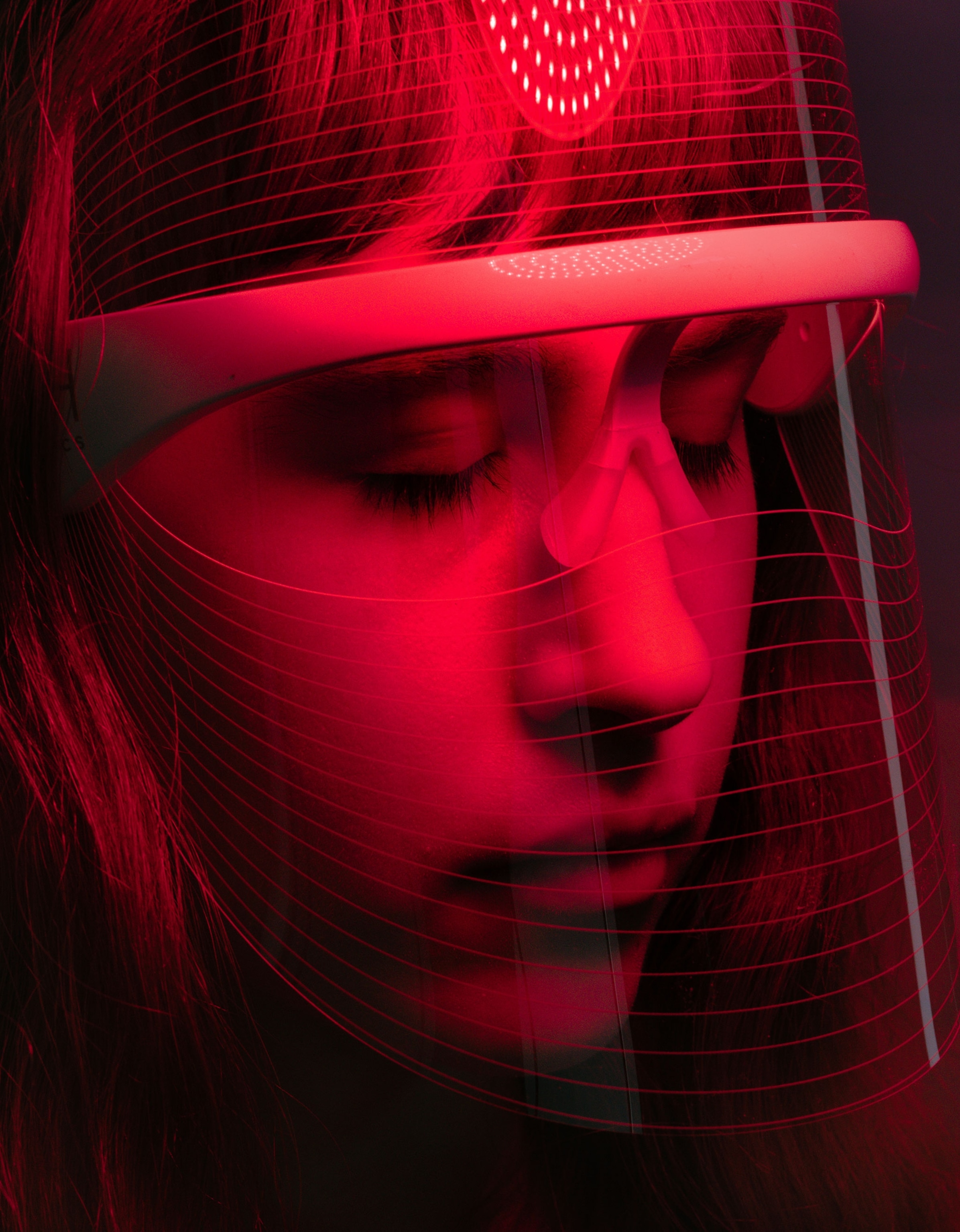 A model poses for a portrait with a LED Light Shield Mask From DM Aesthetics designed for consumer use in a studio against a blue background