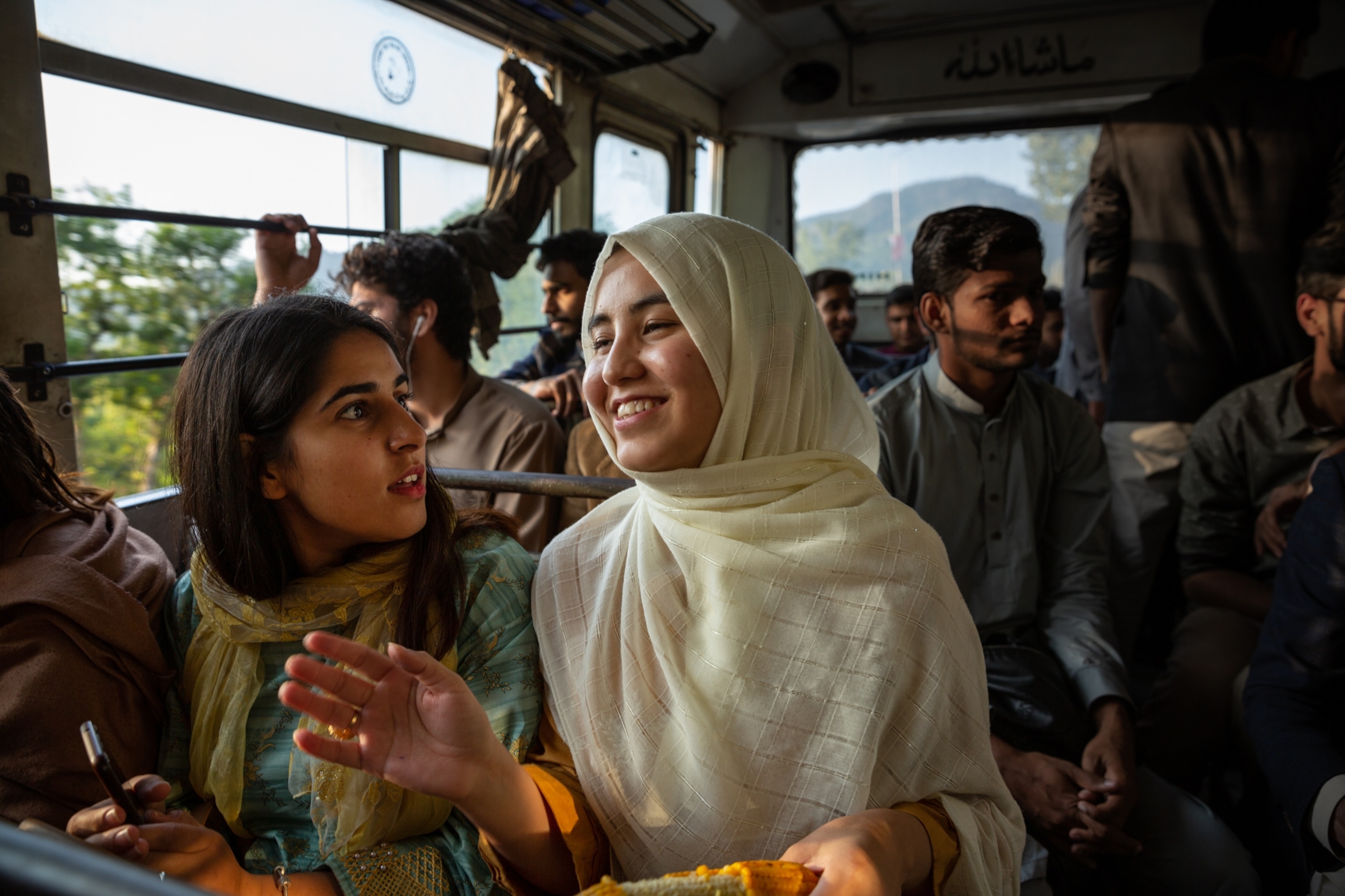two women sitting on a bus, crowded with people