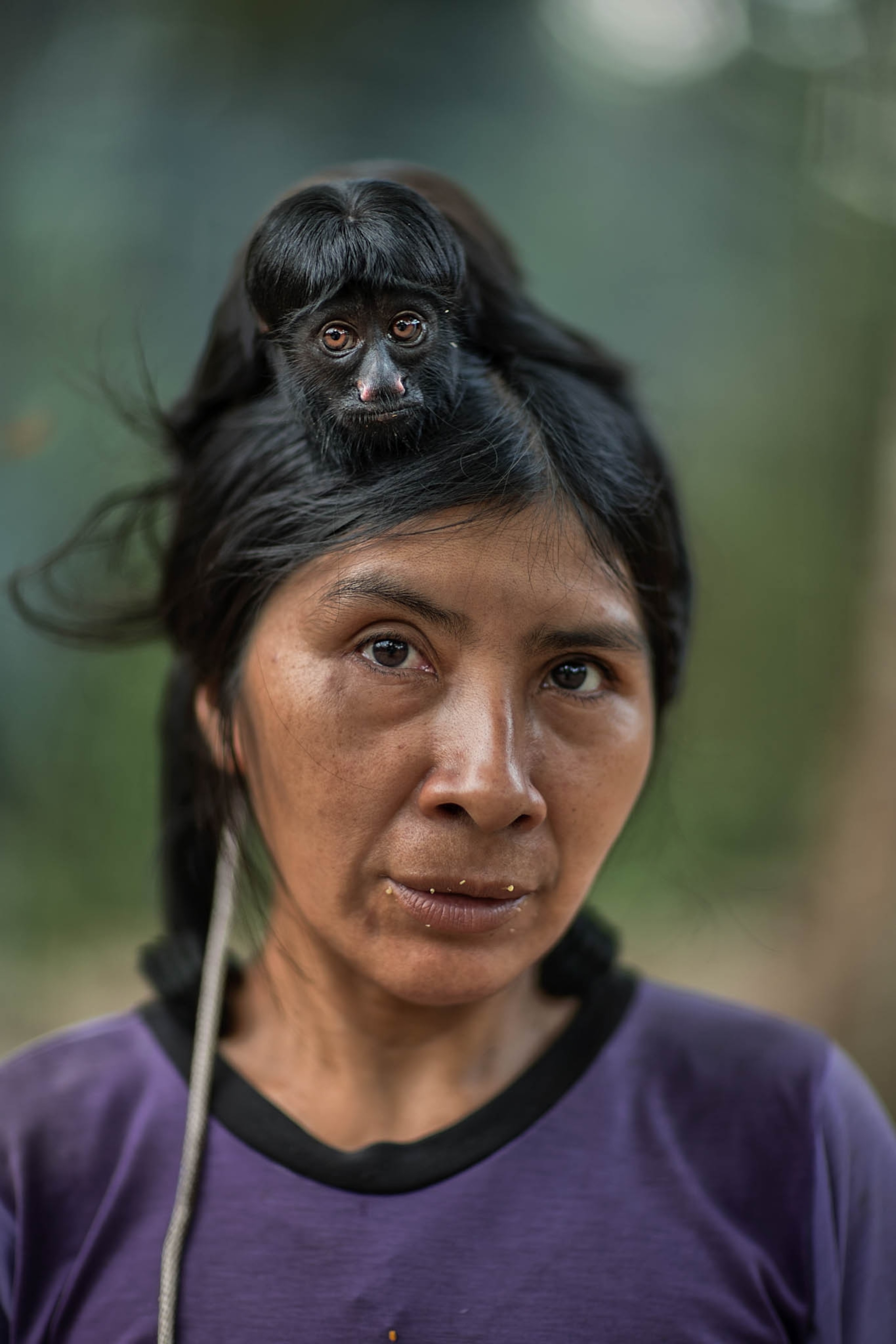 a woman wearing a purple shirt with a small black monkey on her head