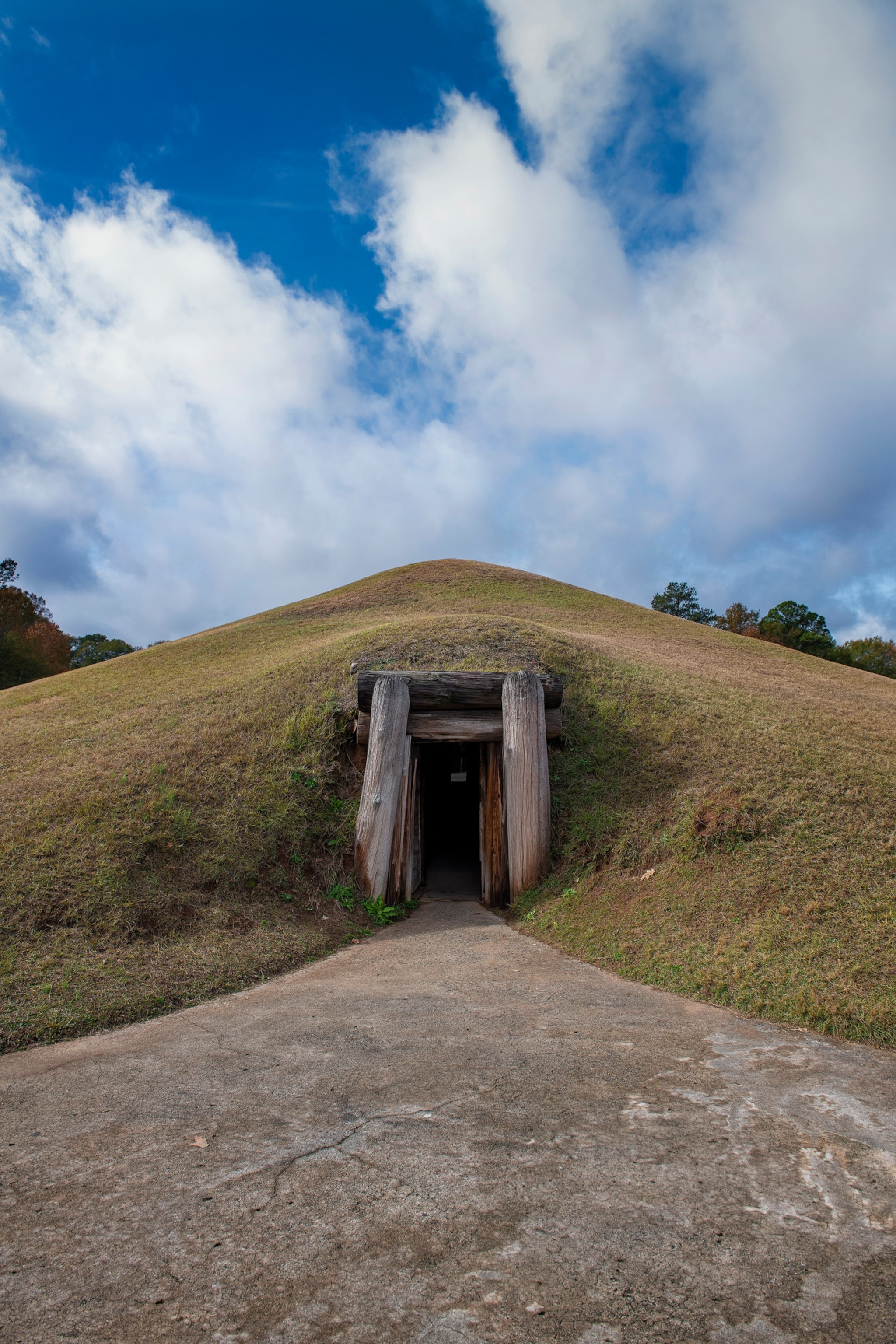 photo of grassy hill, with a path to a wood door to enter the inside the mound.