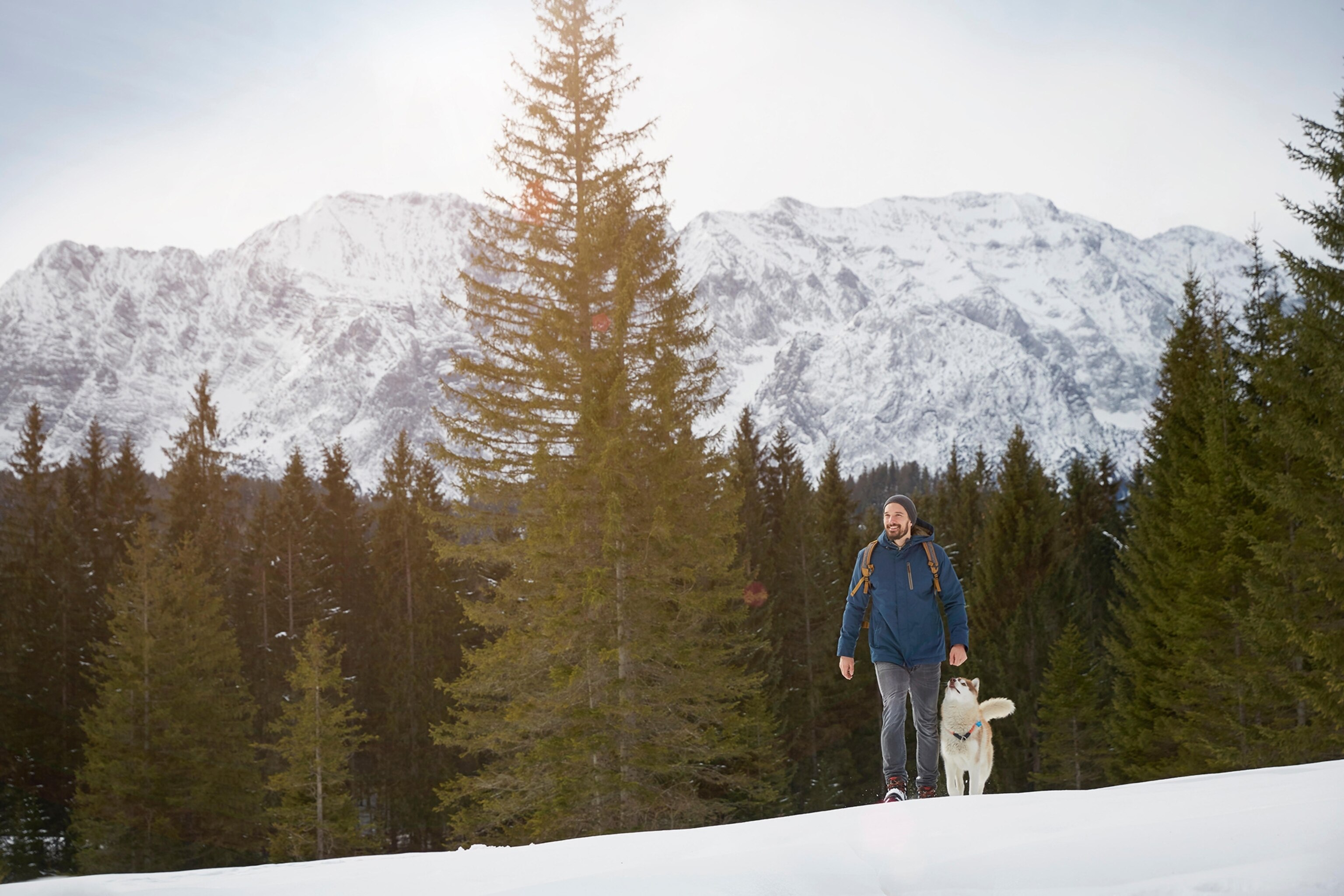 Young man walking uphill with husky in snow covered landscape, Elmau, Bavaria, Germany.
