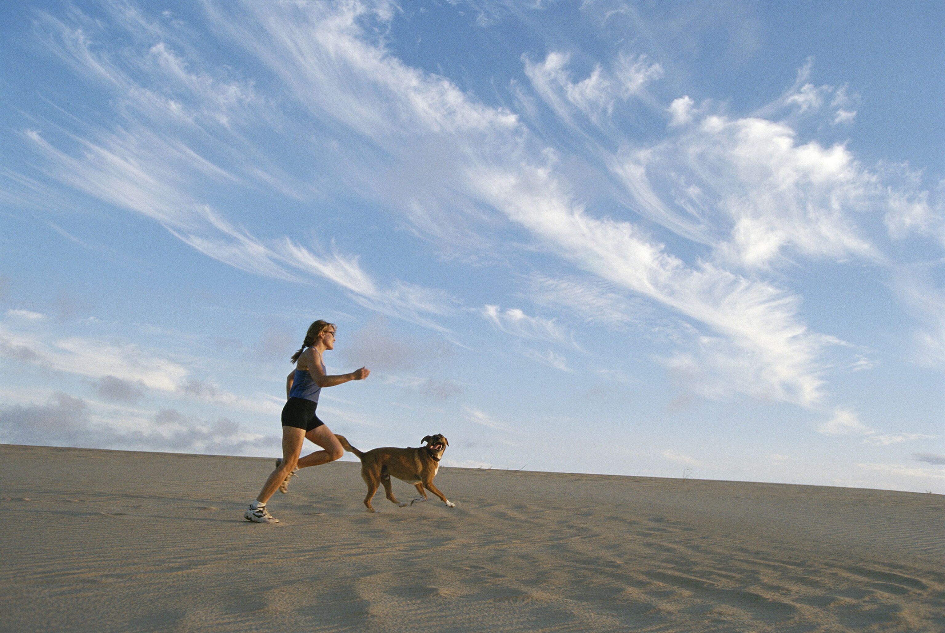 a woman jogging with her dog on a sand dune in Nags Head, North Carolina