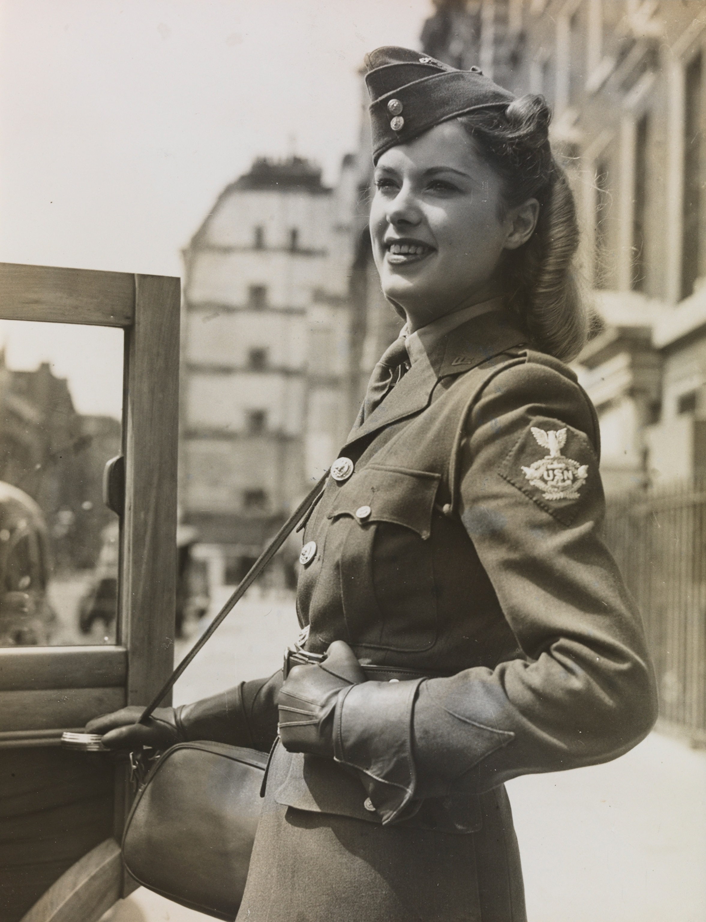 A British woman wearing a khaki uniform stands near a car.