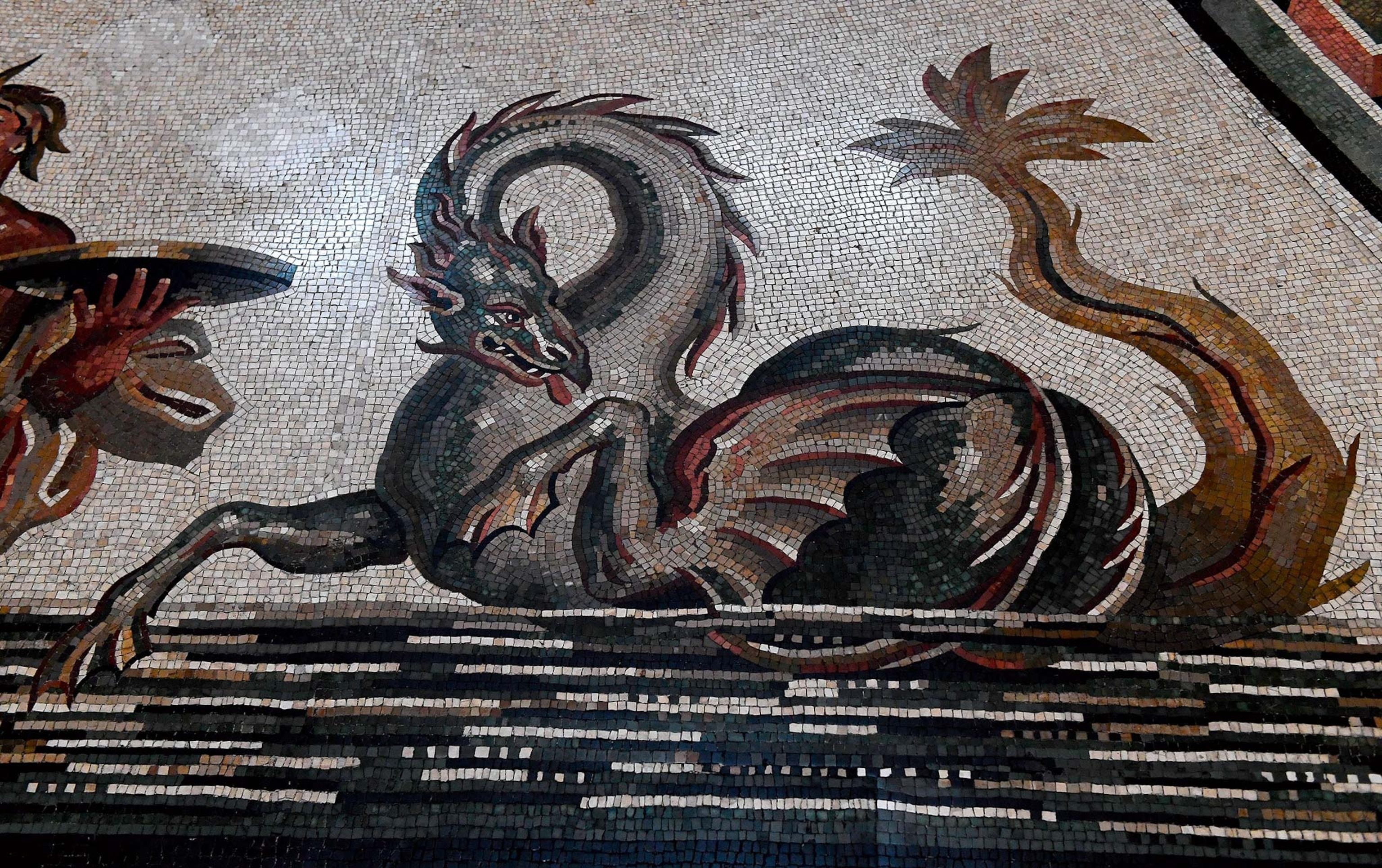 A dragonlike sea monster rears up from a Roman mosaic