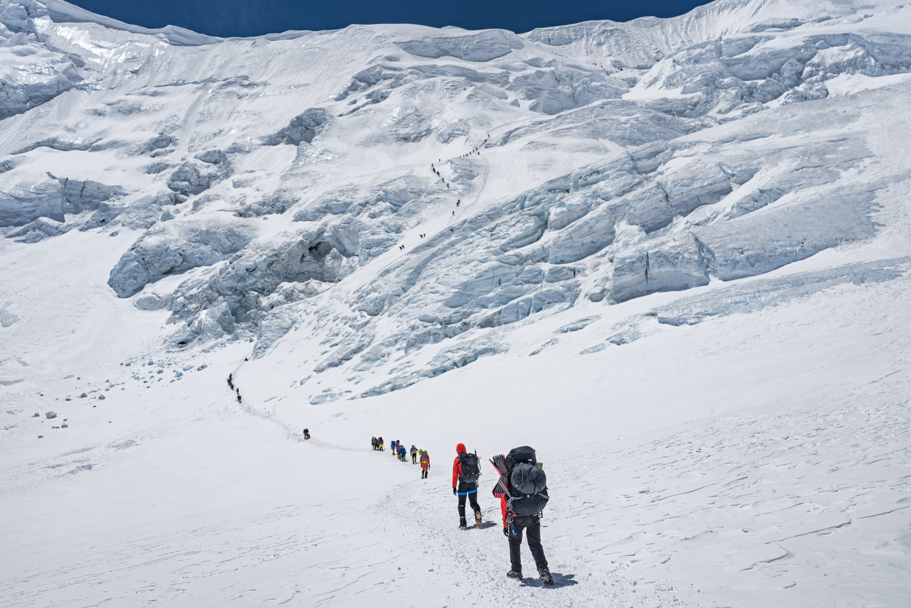 a row of climbers in a single file line walking a flat icy pathway
