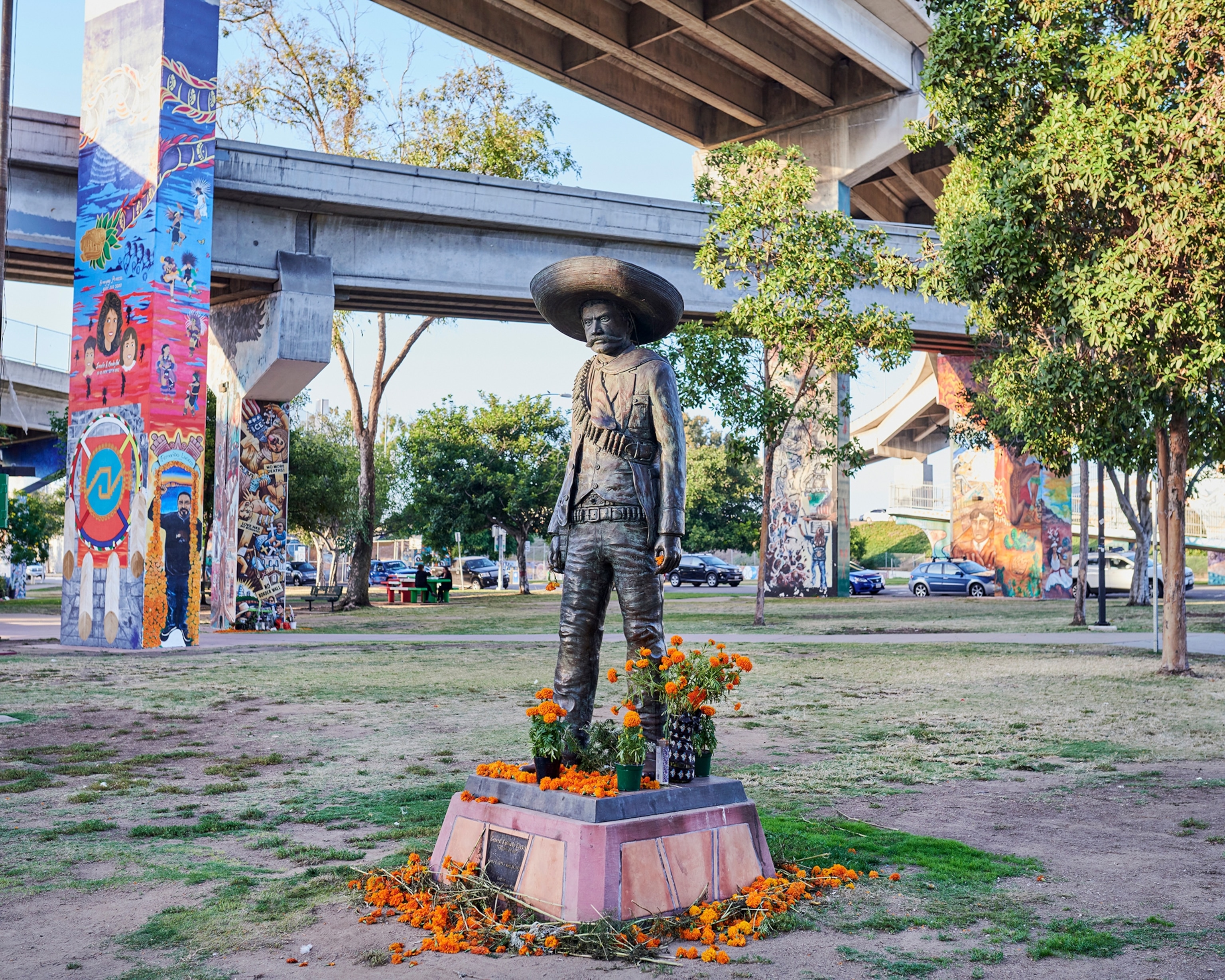 A statue of the Mexican revolutionary Emiliano Zapata at Chicano Park with orange flowers at the base. Colorful murals are painted on the bridge columns.