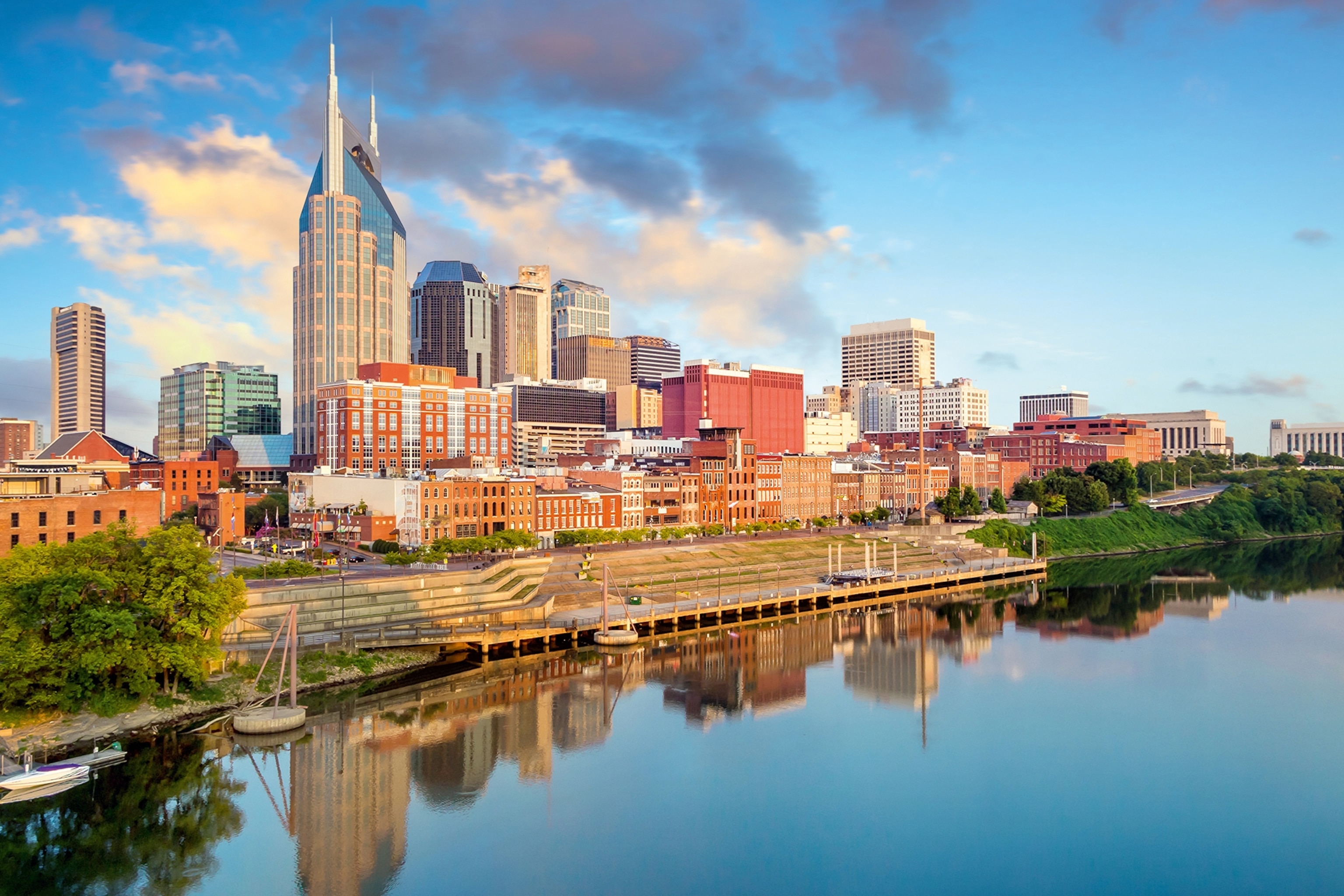 A bright skyline by a wide river with a couple of high-rise buildings and greenery.