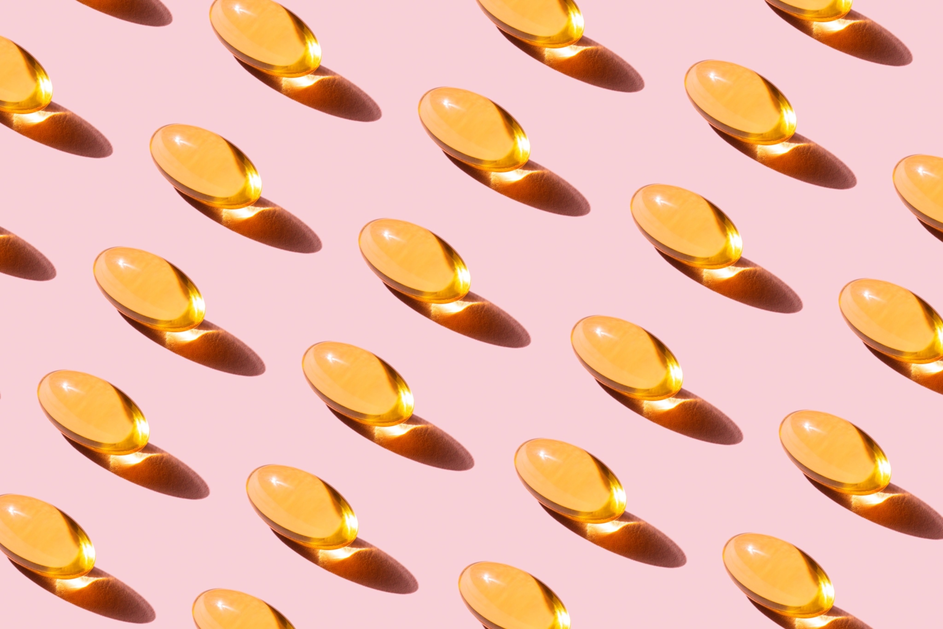 Rows of golden yellow vitamin D capsules, photographed against a ping background