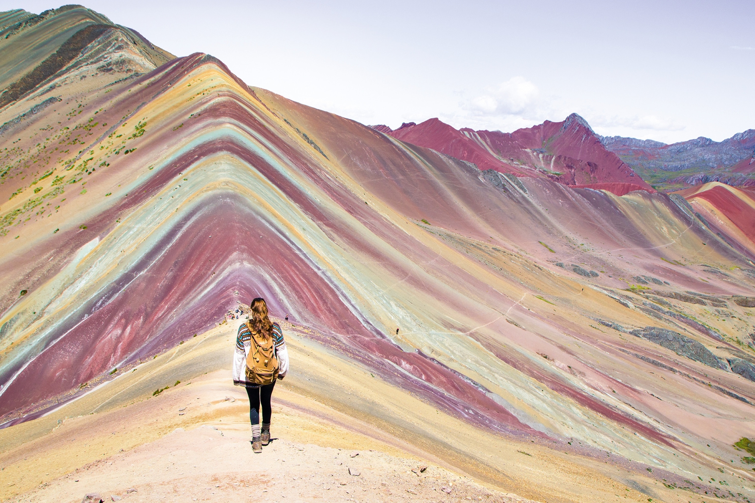 A traveller stands facing Rainbow Mountain - a natural rock formation which has stripes of different colours.