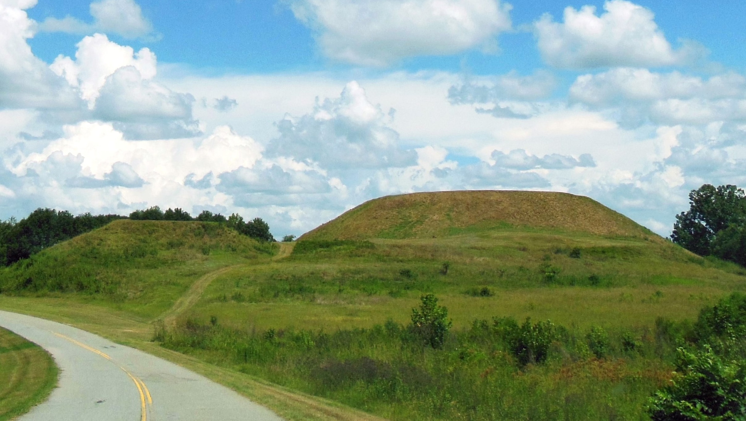 photo of two grassy mounds with a road on the left.