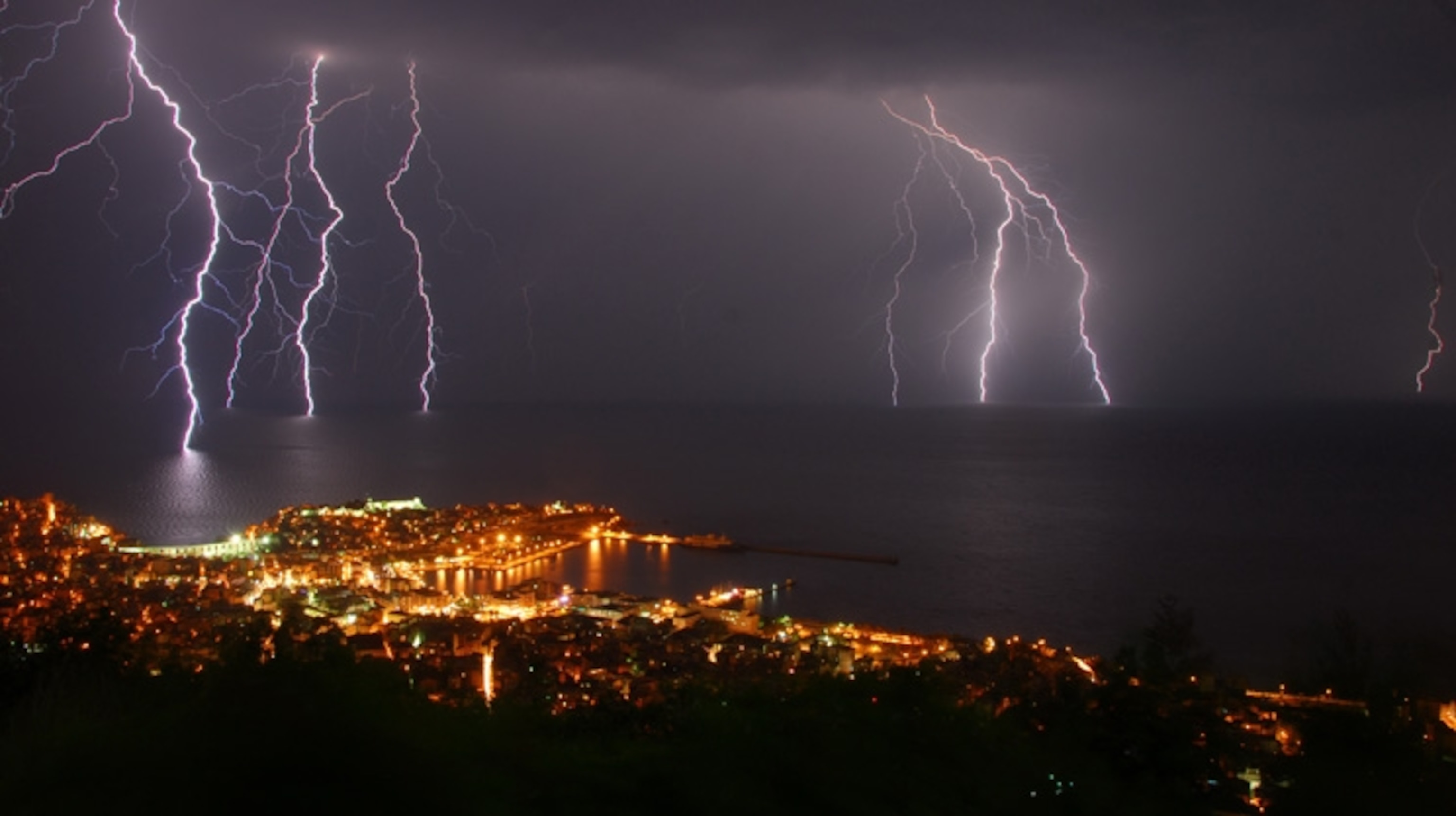 Lightning striking the water off the coast near a city