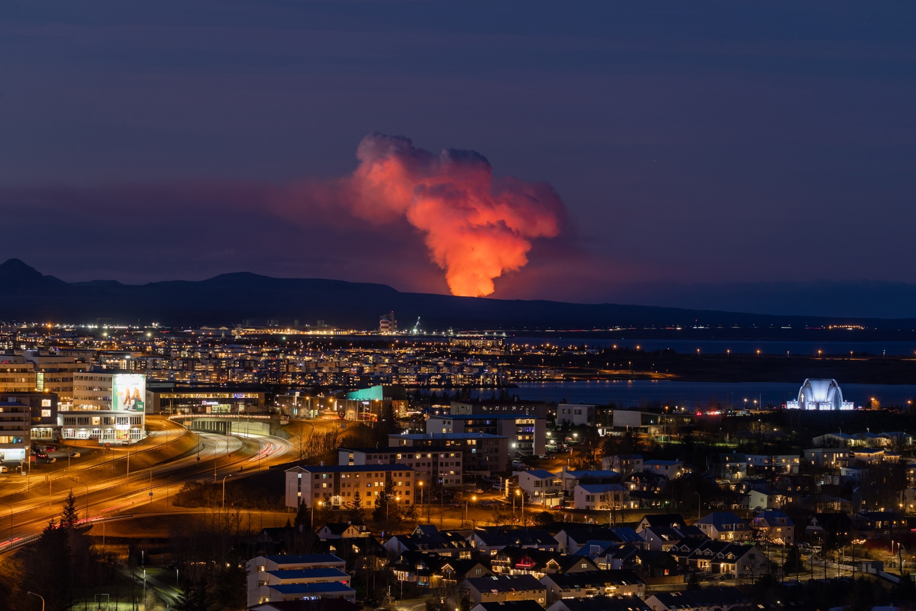 Fire-red smoke is seen billowing towards the sky along the horizon, beyond the city