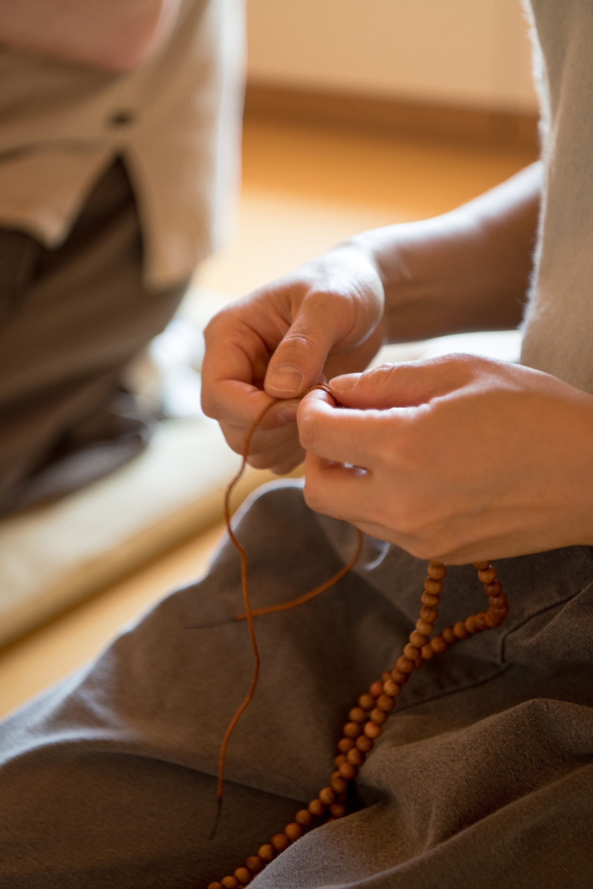 Hands tying a piece of string making a beaded necklace