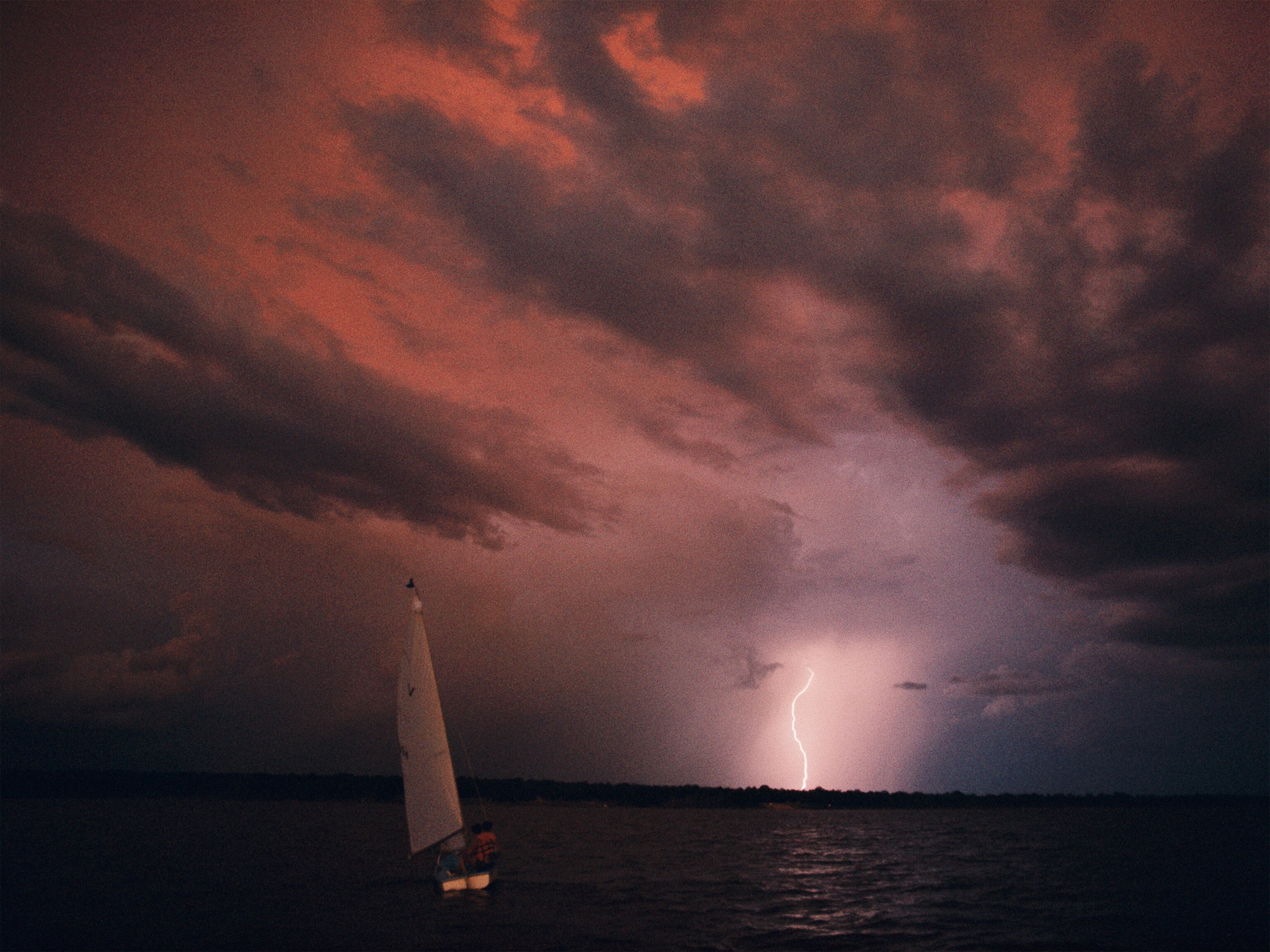 Lightning strikes at twilight near a sailboat in the Chesapeake Bay.
