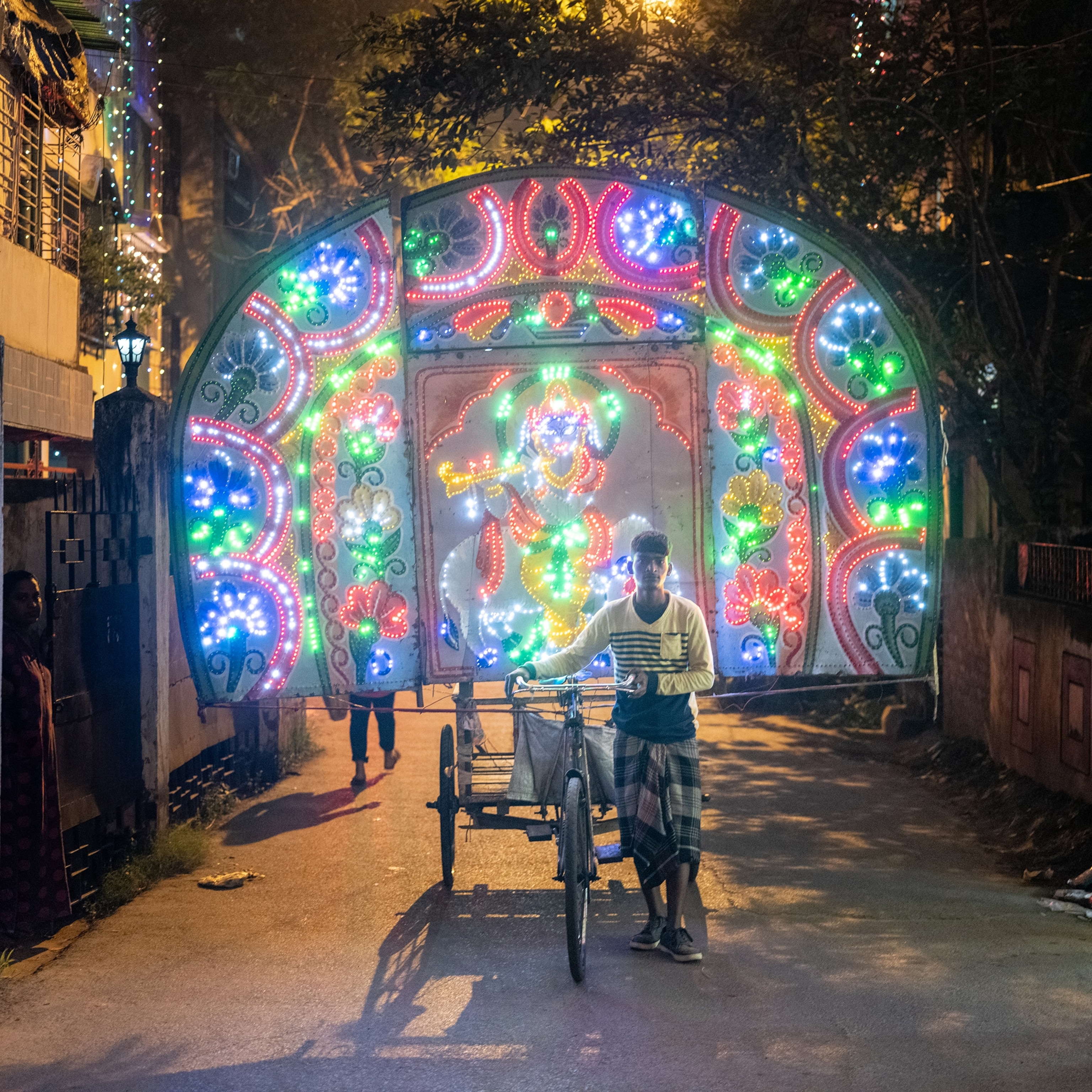A man pulling a large colorful light display during the street celebration of Diwali.