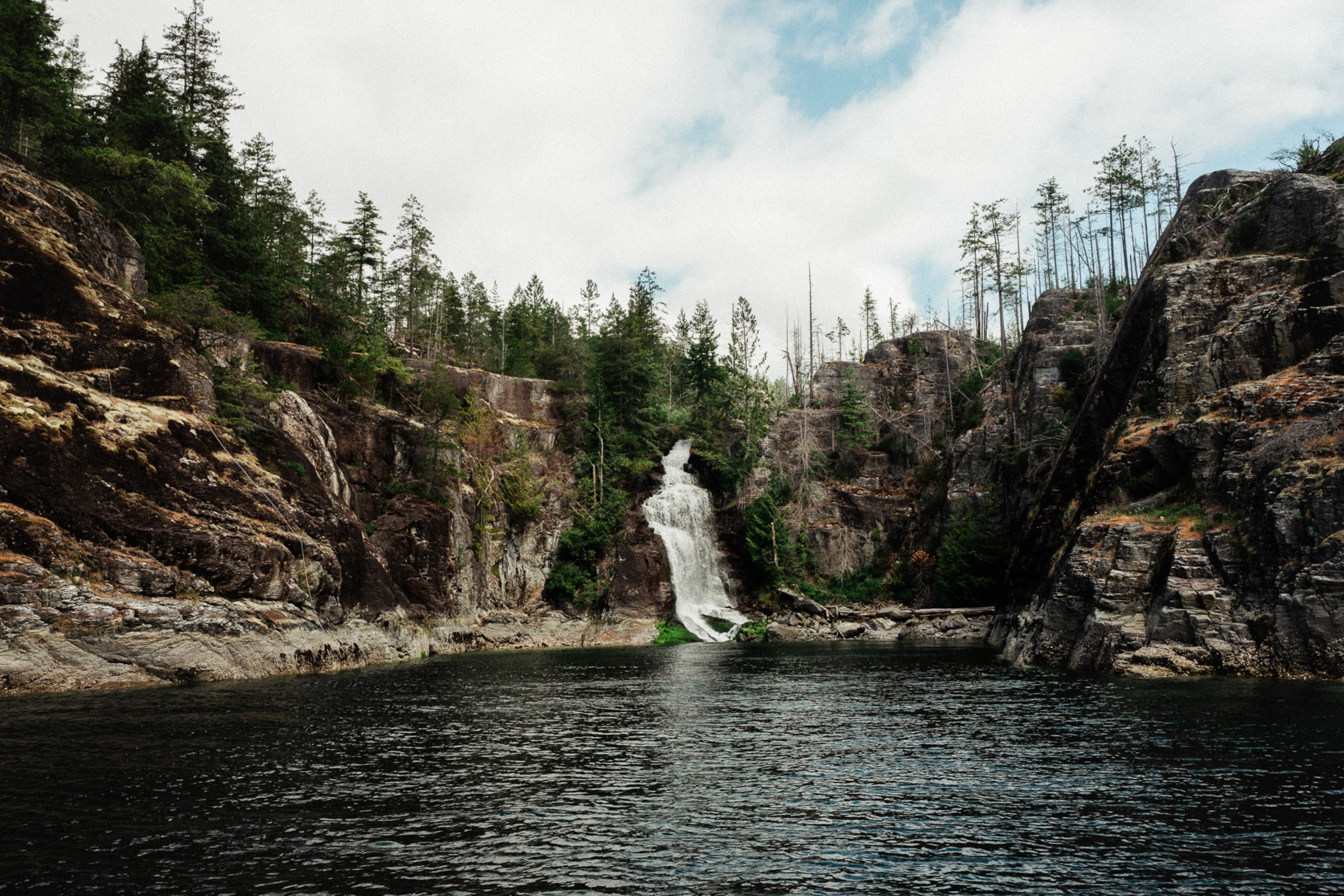 A waterfall cascades down into still waters with trees and cliffs flanking each side.