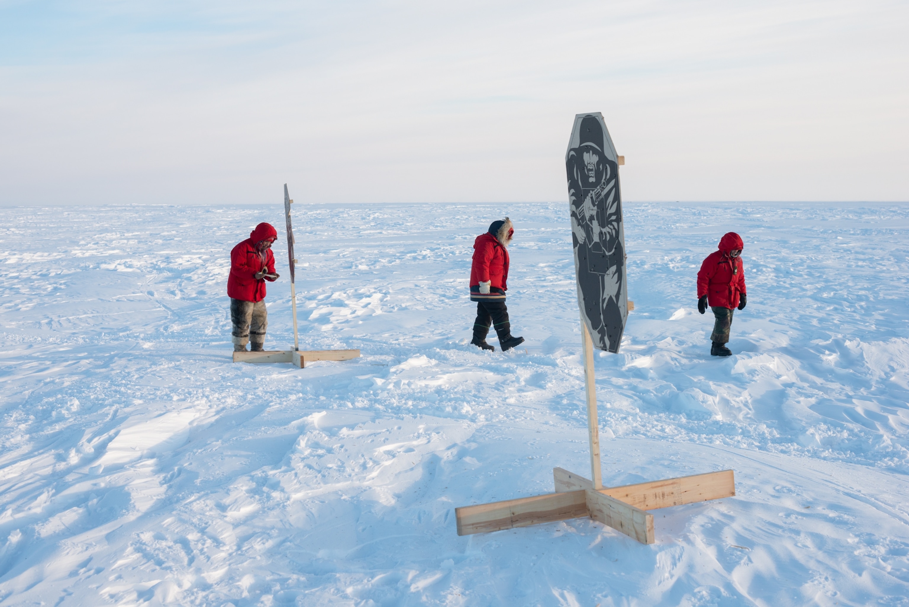 three persons in red coats looking at firing targets.