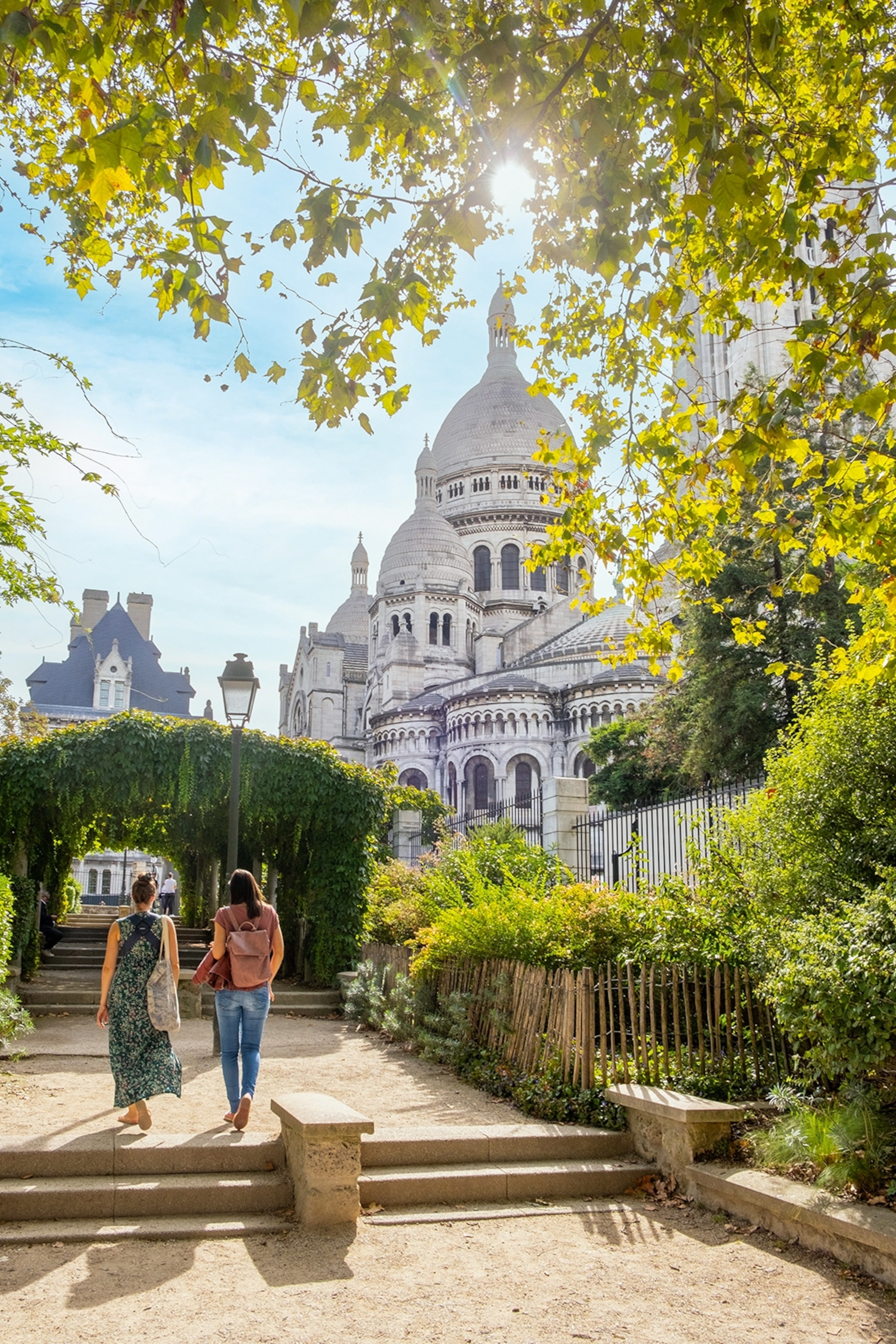 Two women strolling through a Parisian garden with iconic domed buildings in the back